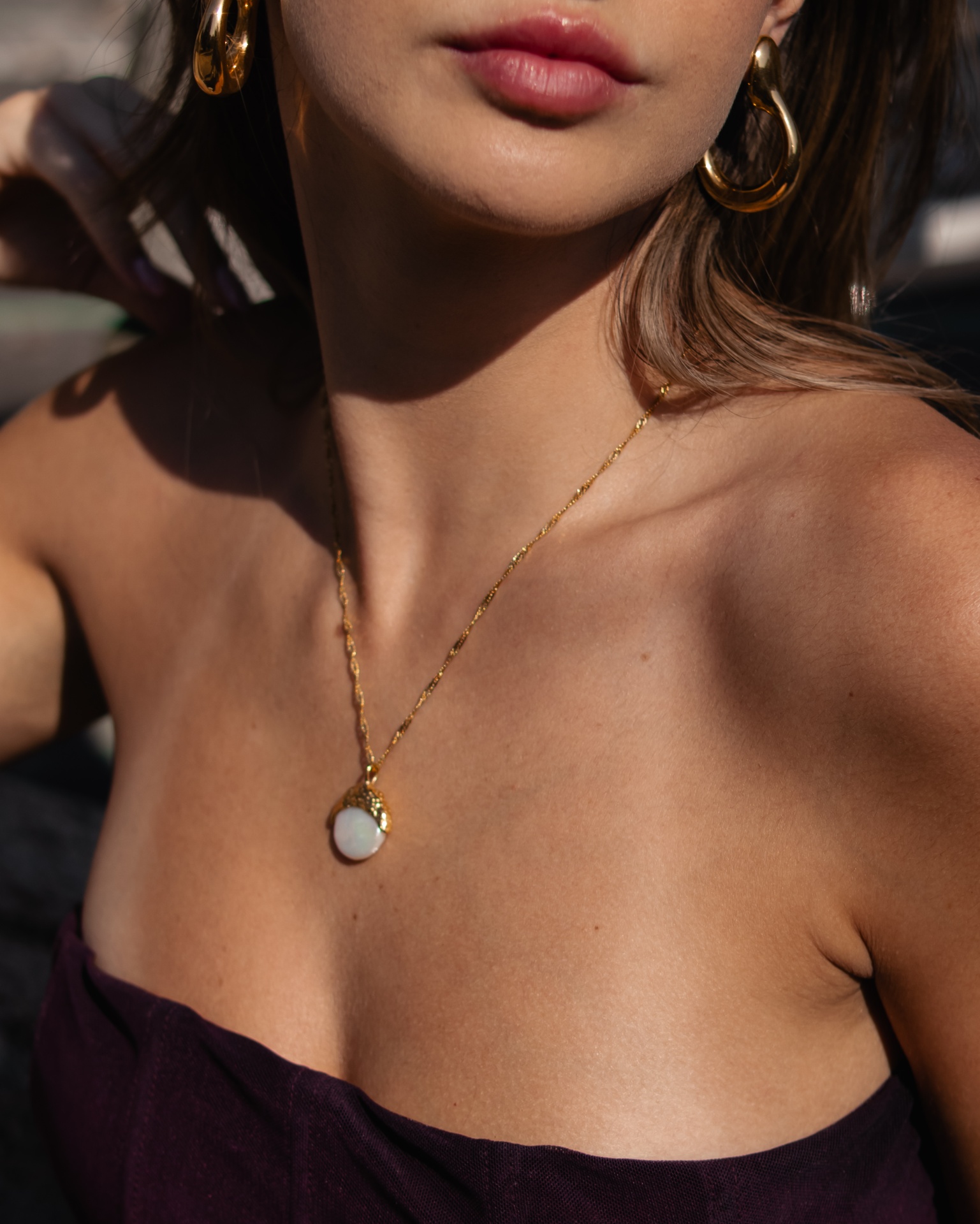 Colar dourado com pendente redondo branco em mulher com brincos de argola dourados