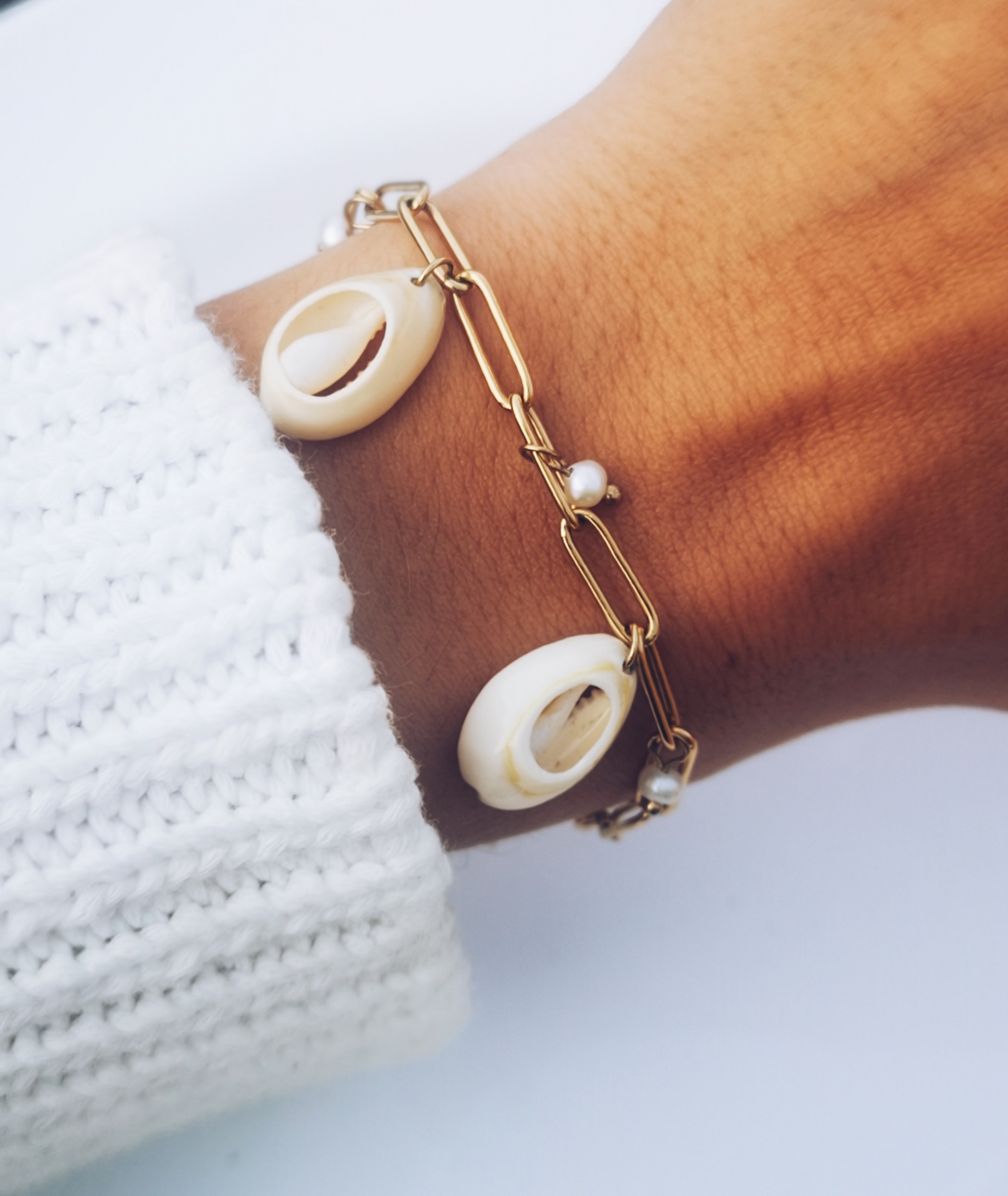 Pulseira dourada com conchas e pérolas no pulso