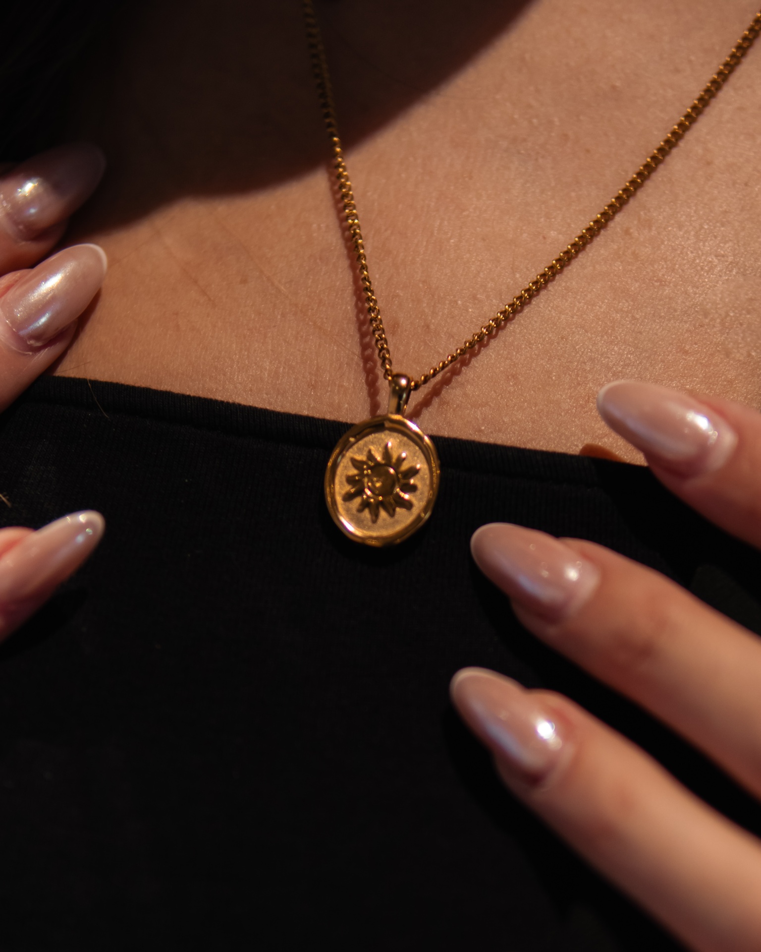 Colar dourado com pendente em forma de sol e unhas compridas nude