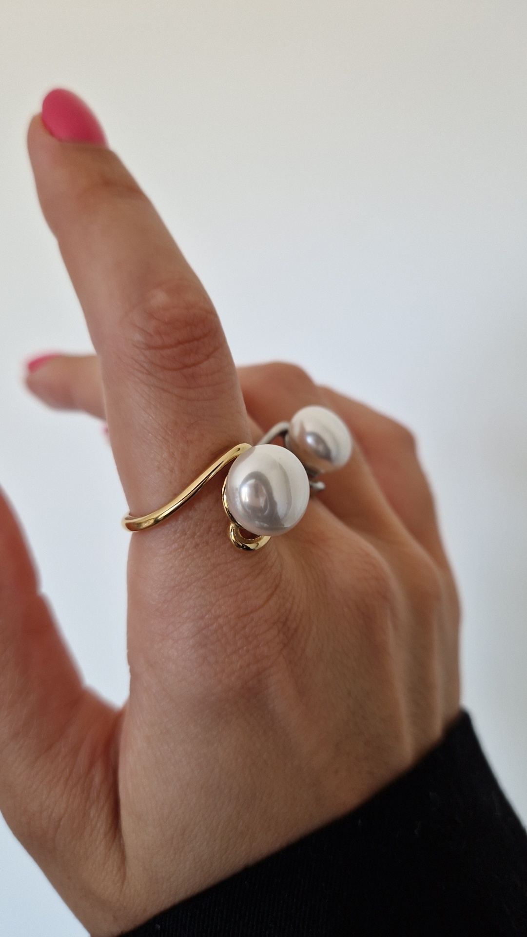 Anel dourado com pérolas numa mão com unhas rosa