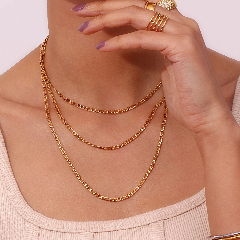 Pescoço com três colares dourados e mão com anéis dourados e unhas roxas