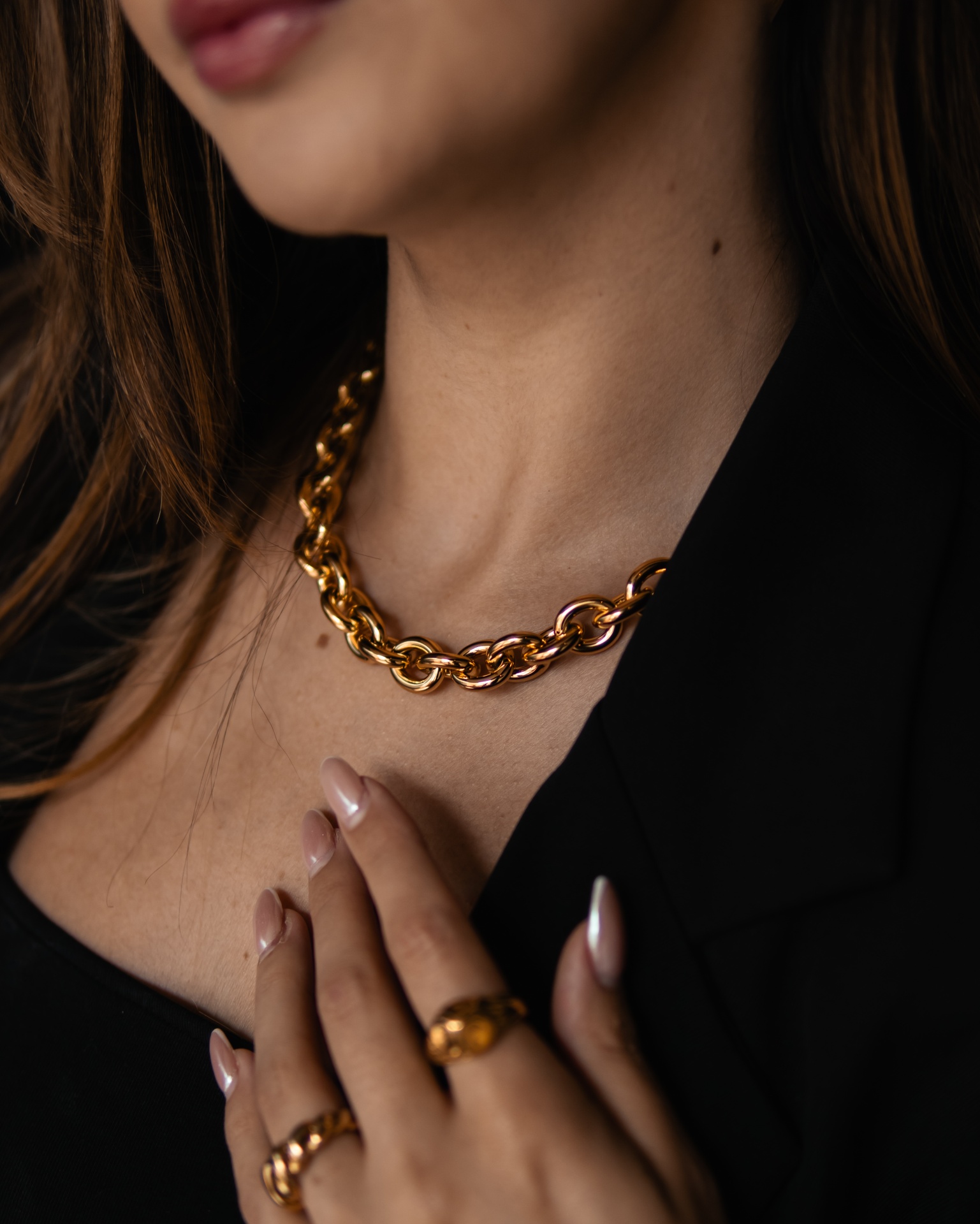 Colar e anéis dourados de elos grossos numa mulher com casaco preto