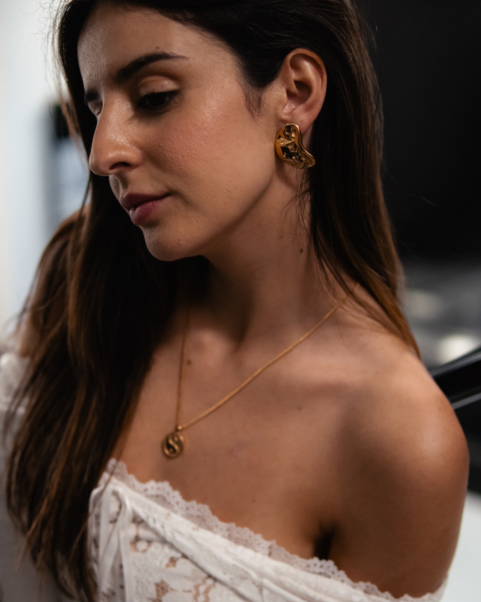 Colar e brincos dourados abstratos em mulher com blusa branca.