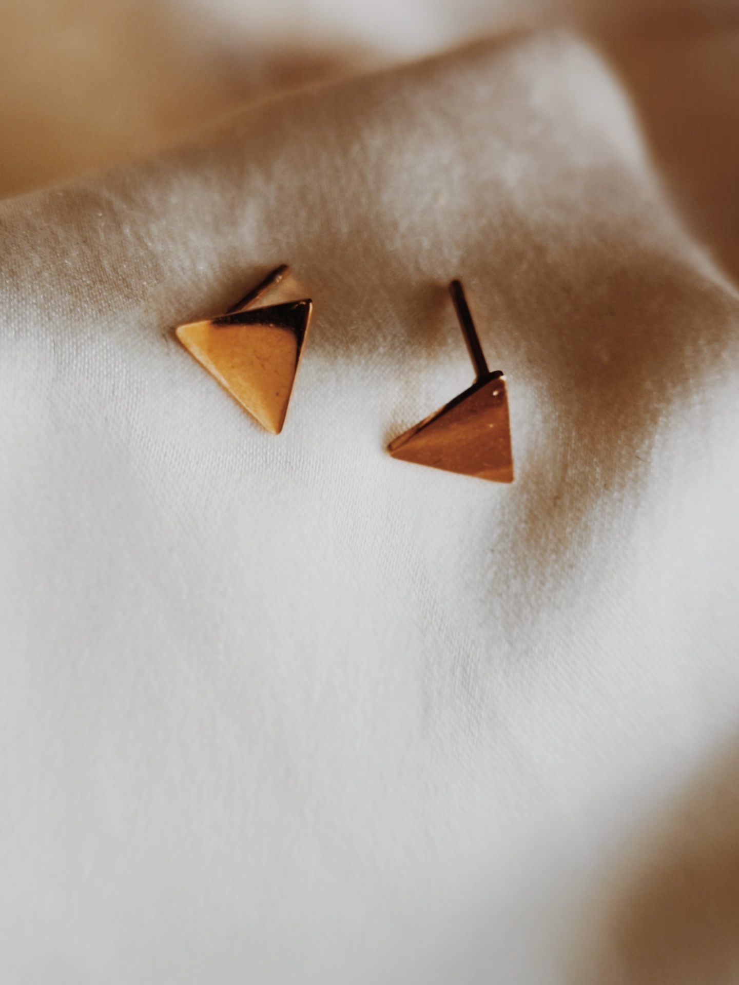 Brincos triangulares dourados sobre tecido branco