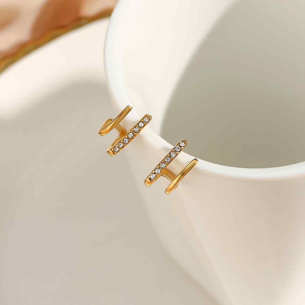 Brincos dourados com pedras junto a chávena branca