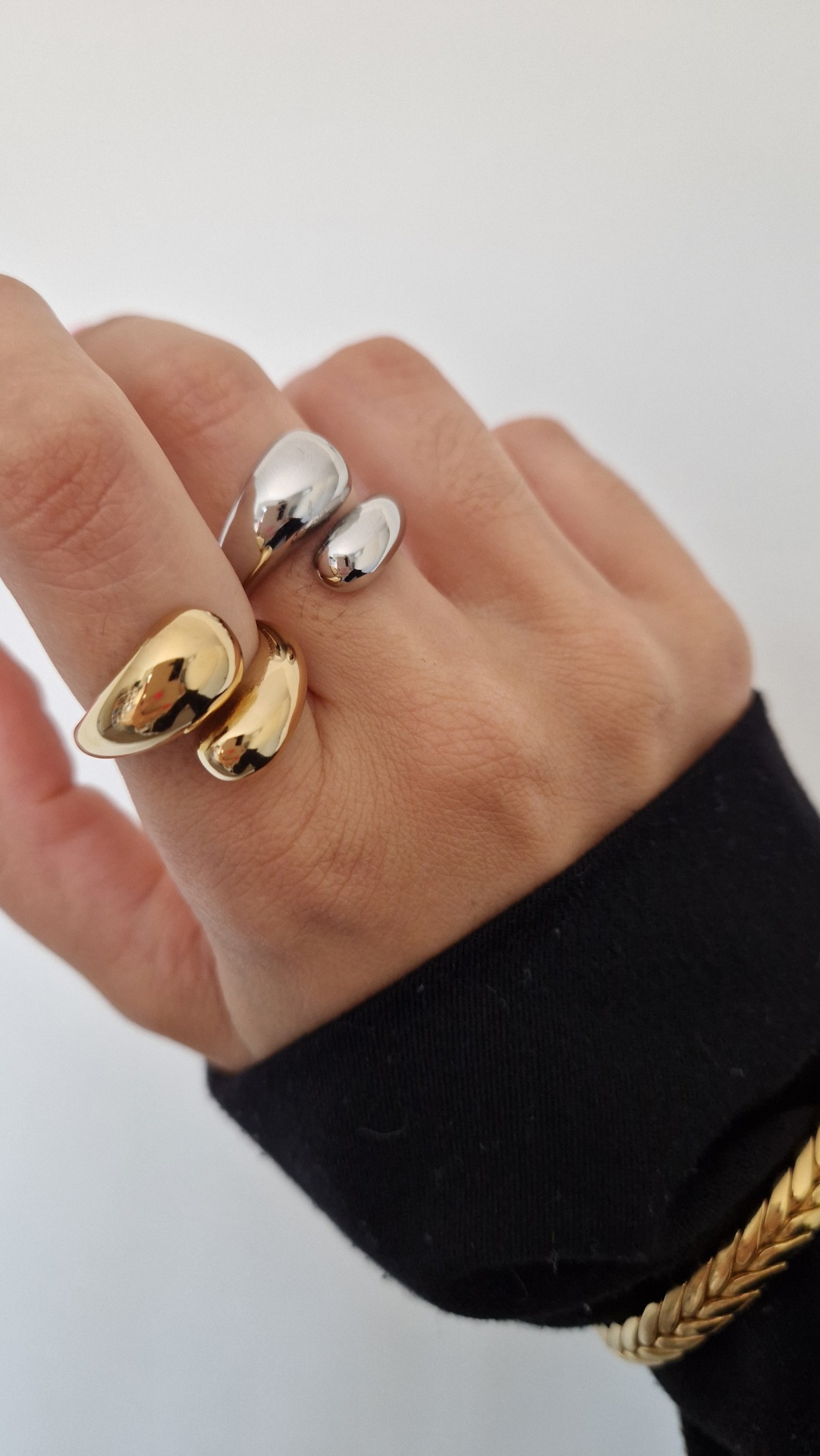 Anel aberto dourado e prateado em mão com manga preta e pulseira dourada
