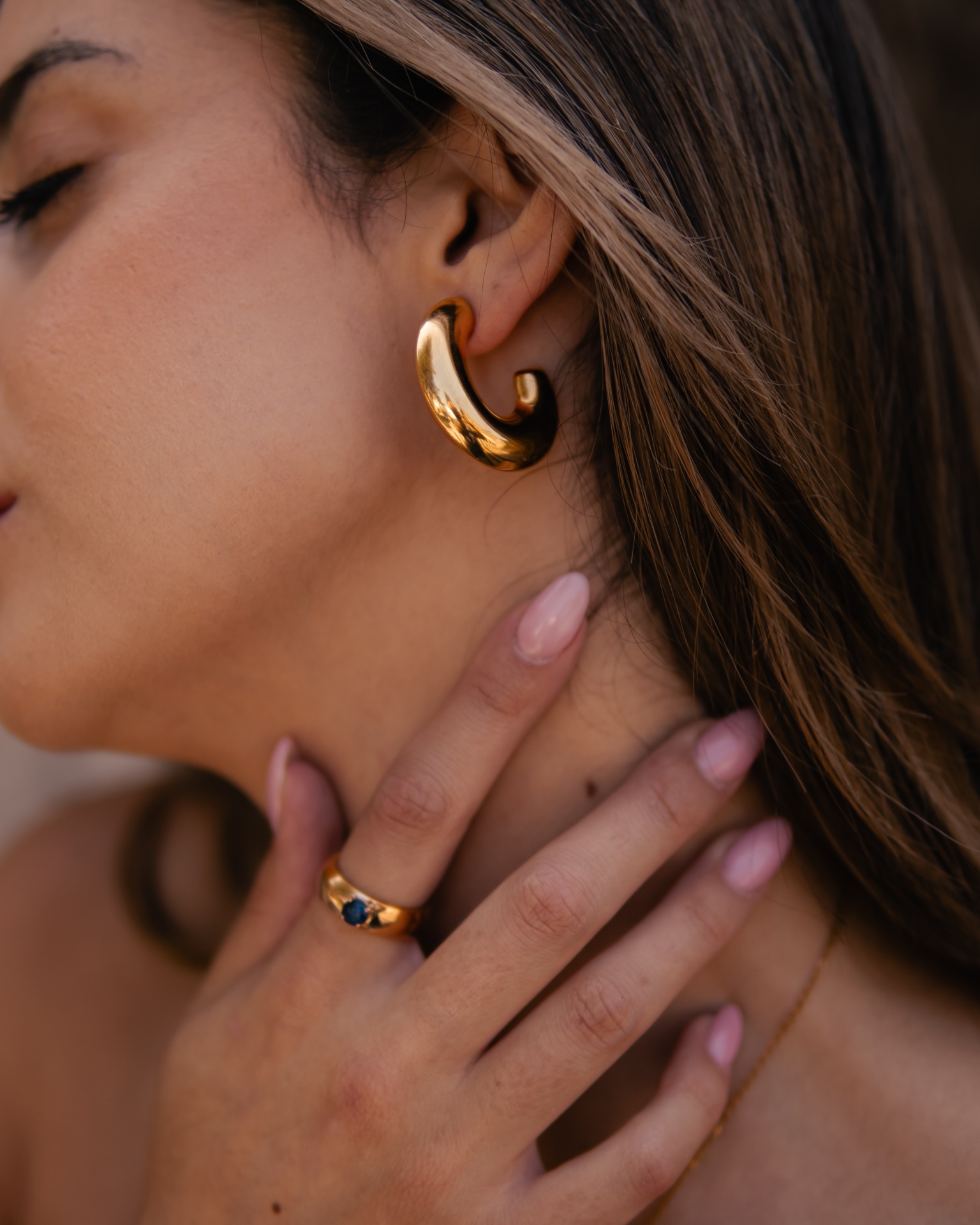 Brincos dourados e anel com pedra azul usados por mulher