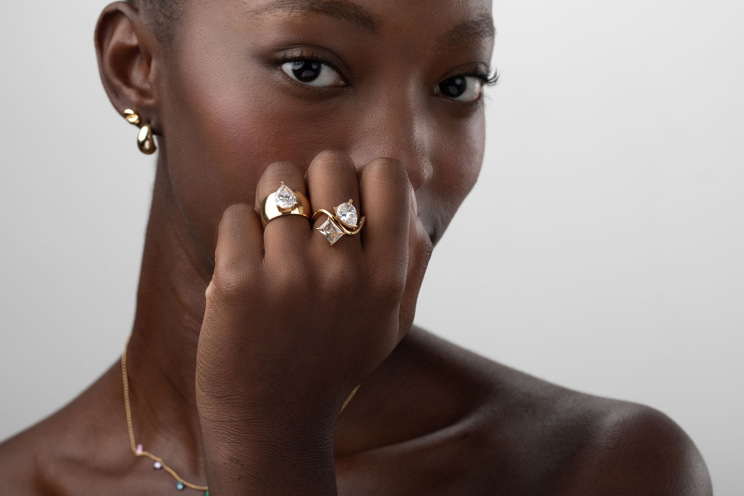 Mulher com brincos dourados, dois anéis com pedras transparentes e colar colorido