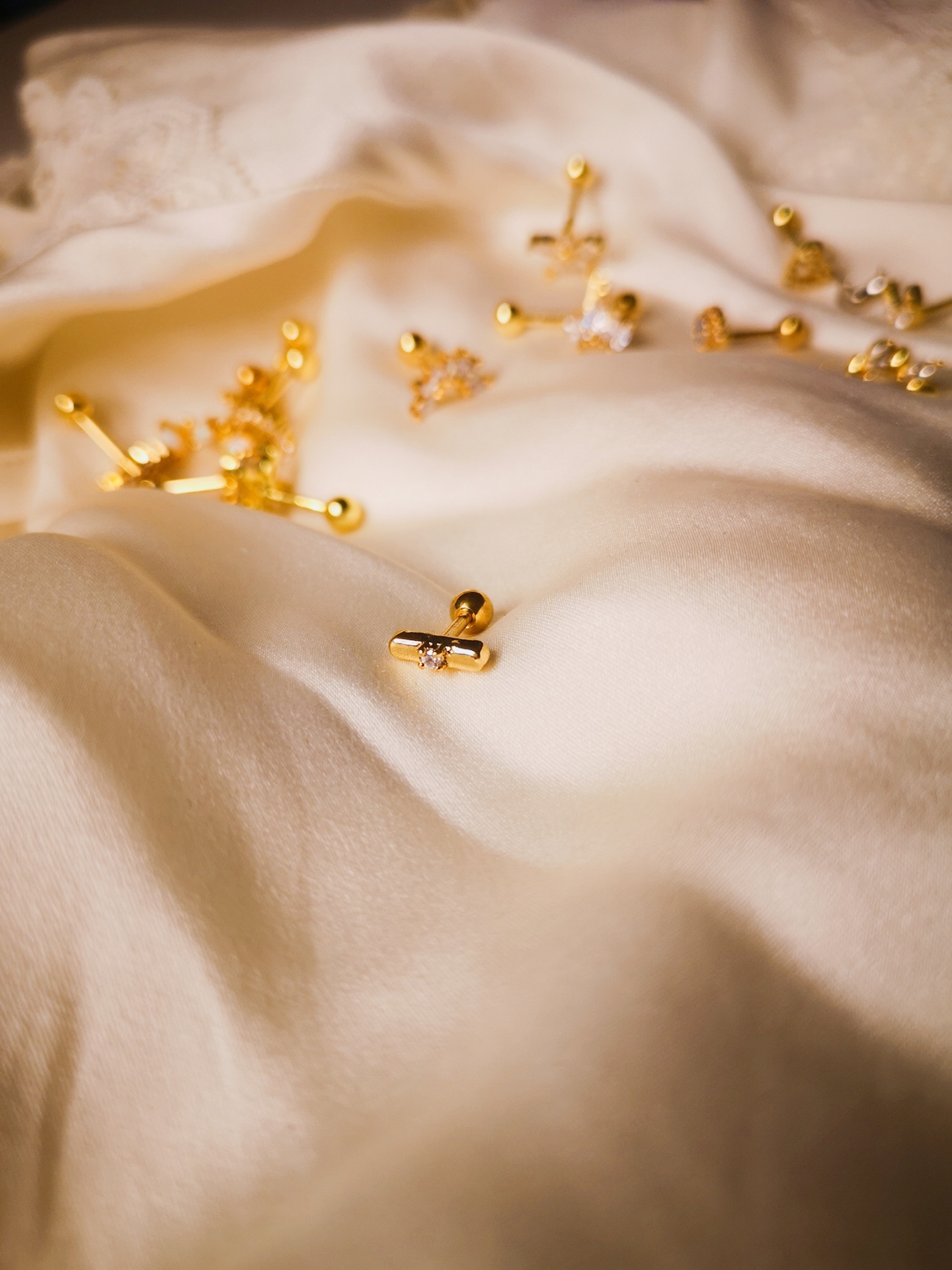 Brincos dourados sobre tecido branco acetinado e renda