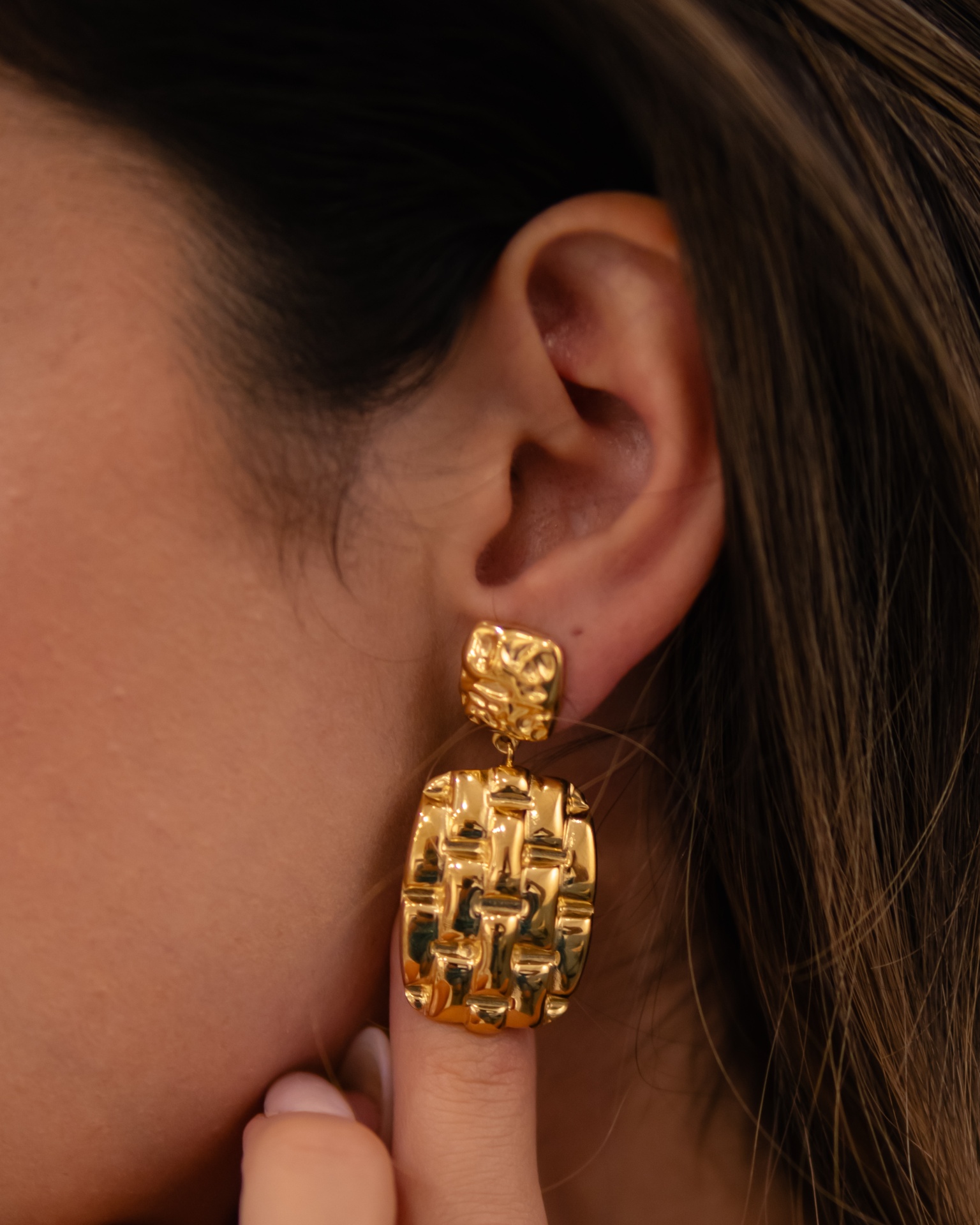 Brinco dourado texturizado com padrão geométrico em orelha