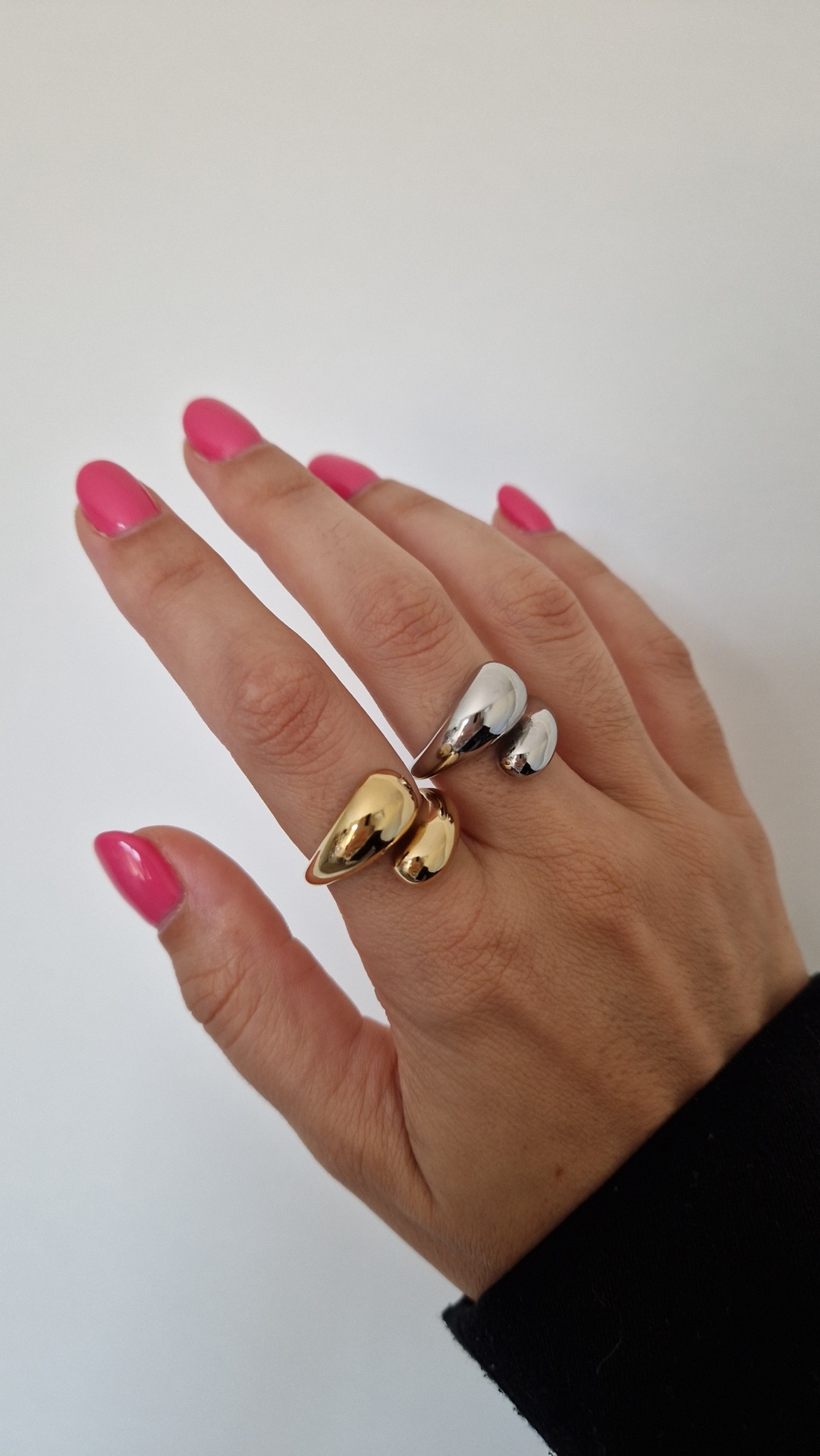 Mão feminina com anéis dourado e prateado e unhas rosa