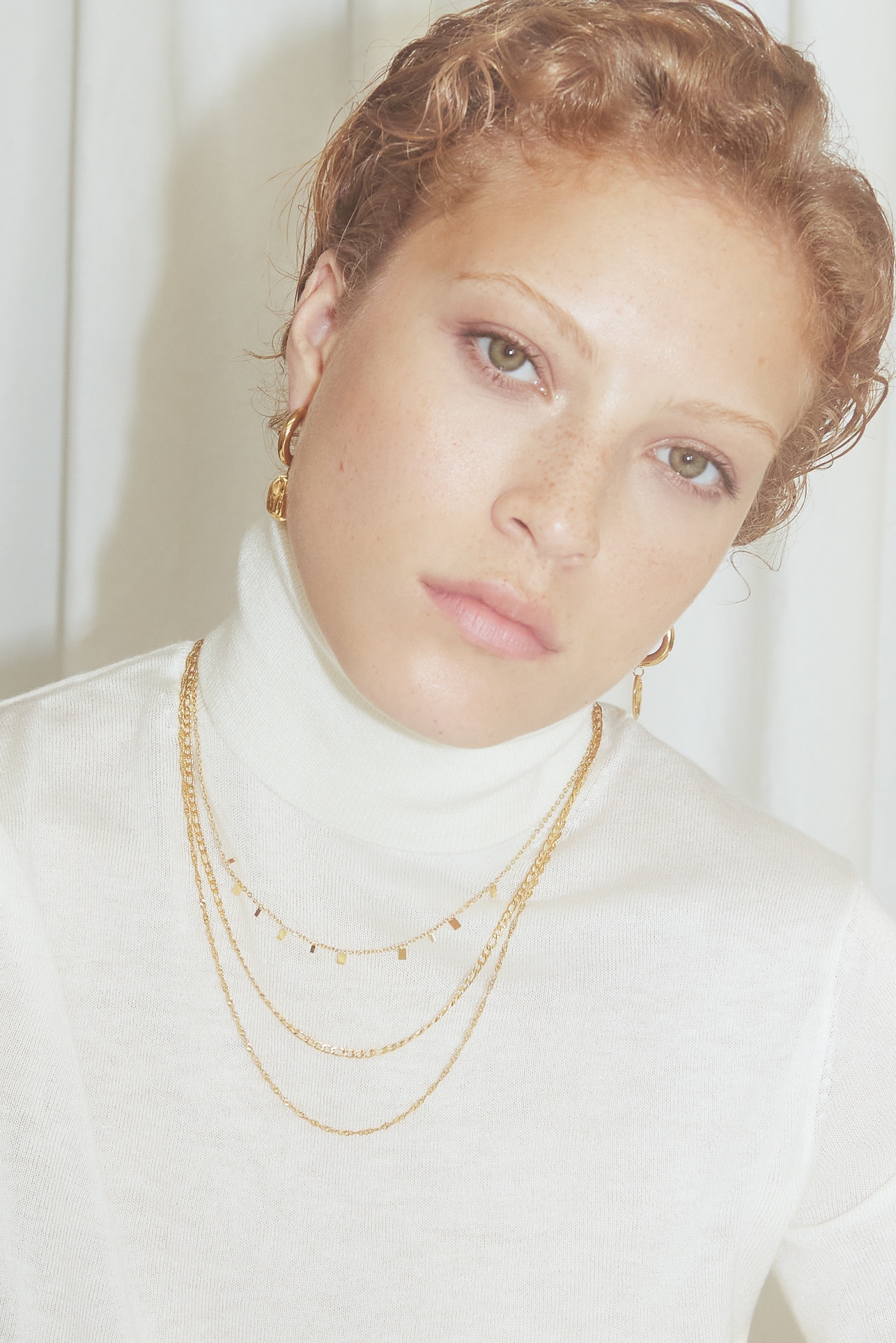 Mulher com colar triplo dourado e camisola branca de gola alta