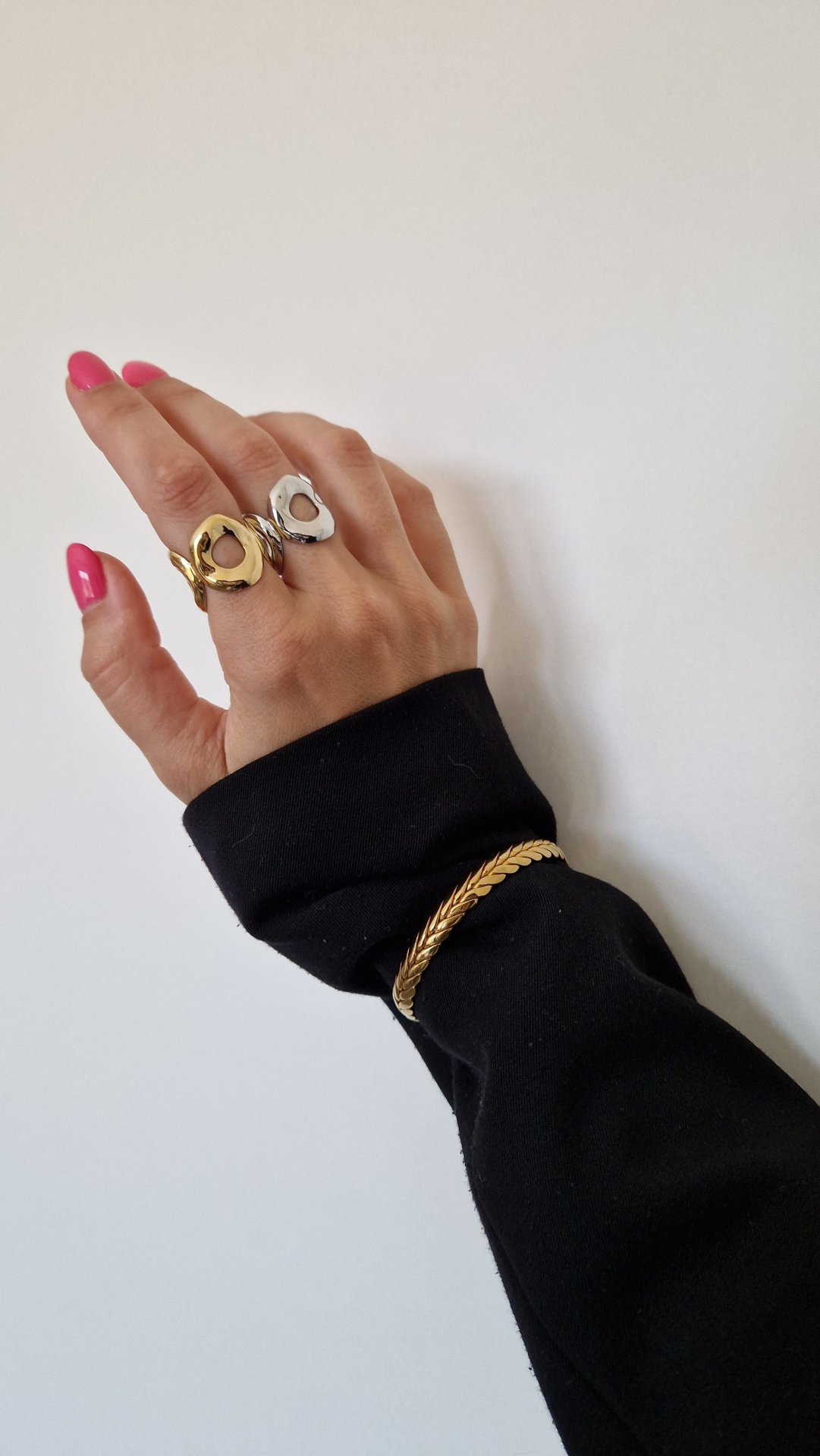 Mão com anéis dourado e prateado e pulseira dourada sobre manga preta