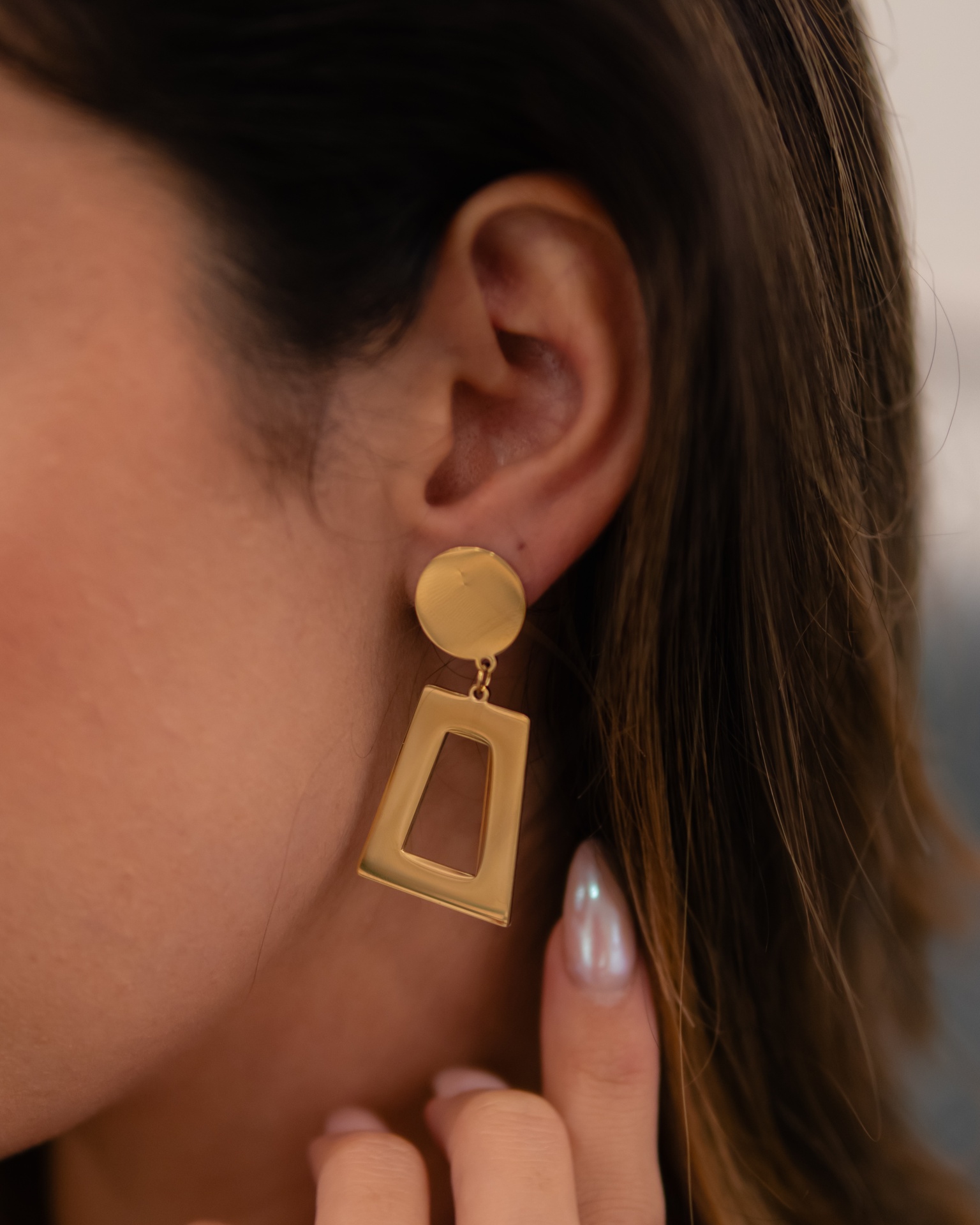 Brinco dourado pendente com base circular e trapezoidal recortado na orelha direita