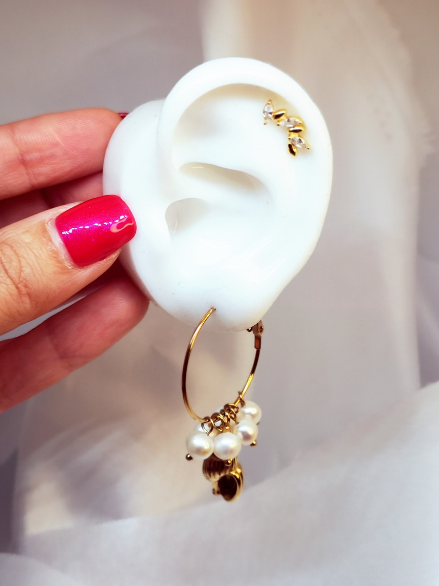 Brinco de argola dourada com pérolas e detalhes metálicos em modelo de orelha