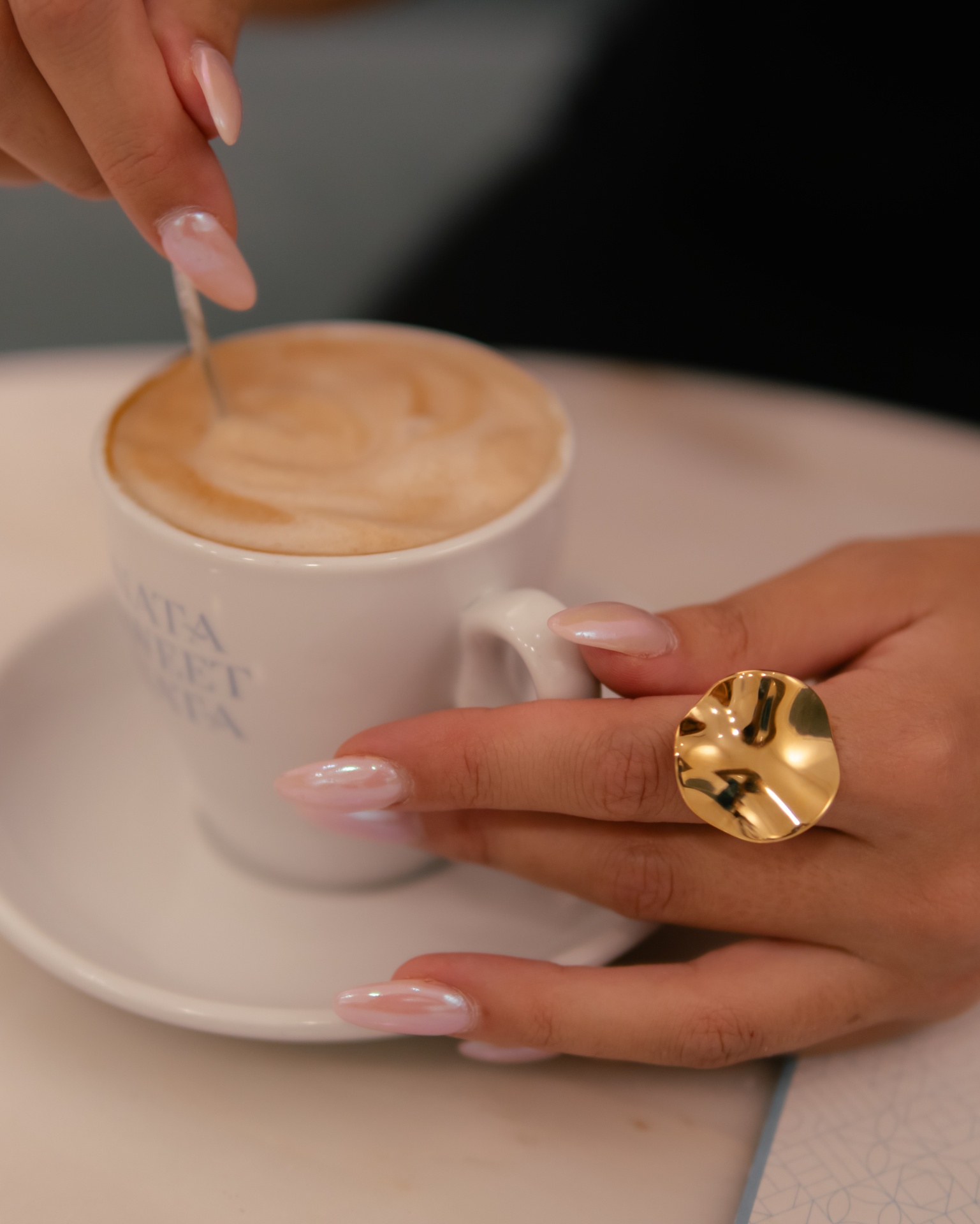 Mão com anel dourado a segurar caneca branca com sopa cremosa