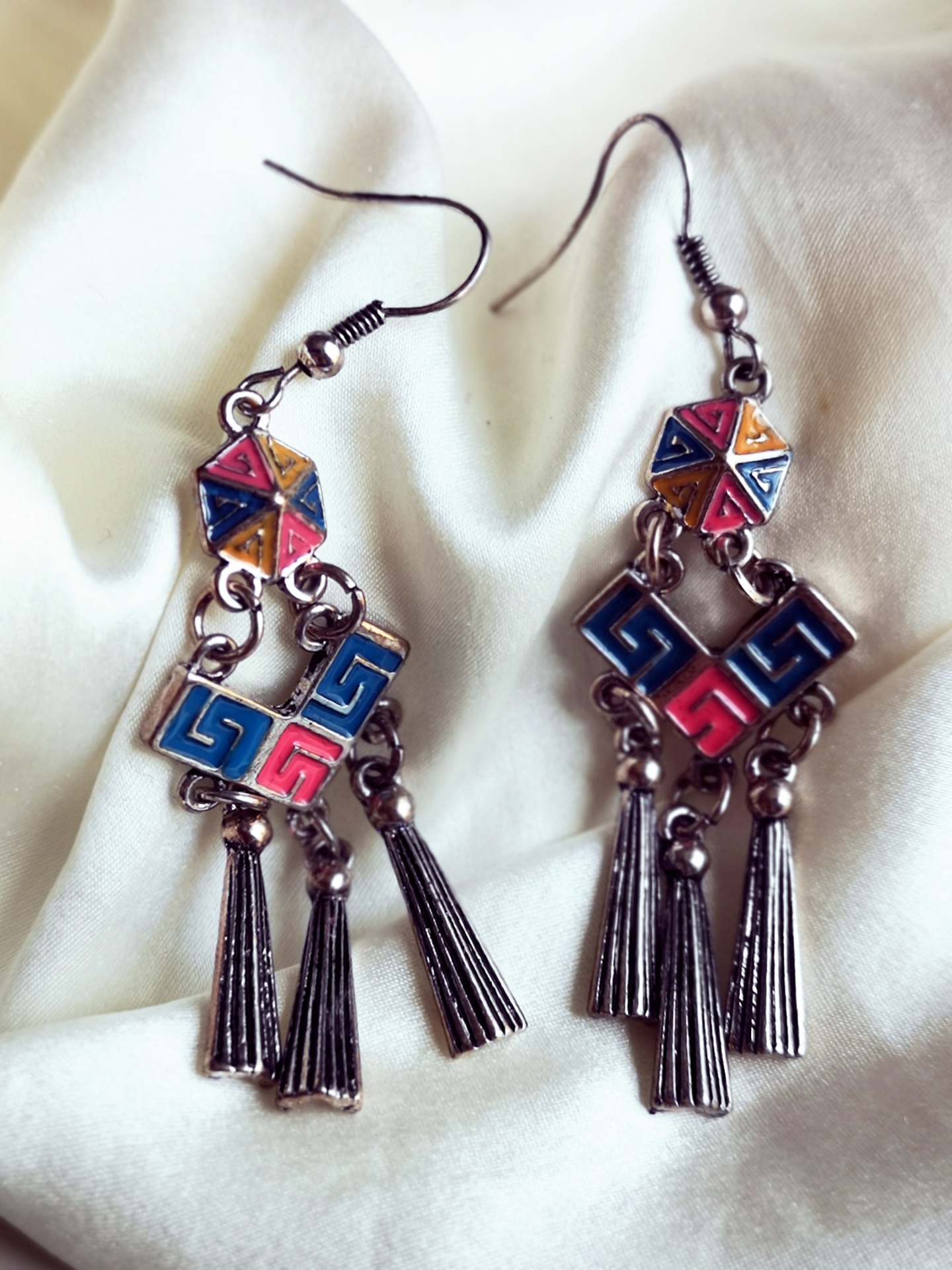 Brincos metálicos pendentes com padrões geométricos coloridos e franjas