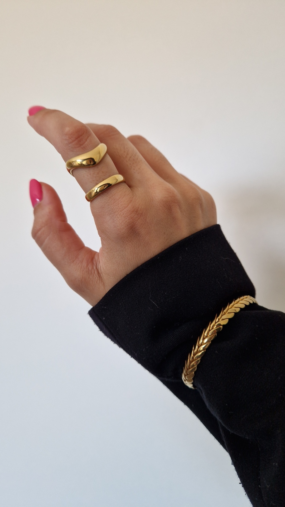 Mão com argolas douradas e pulseira dourada sobre manga preta