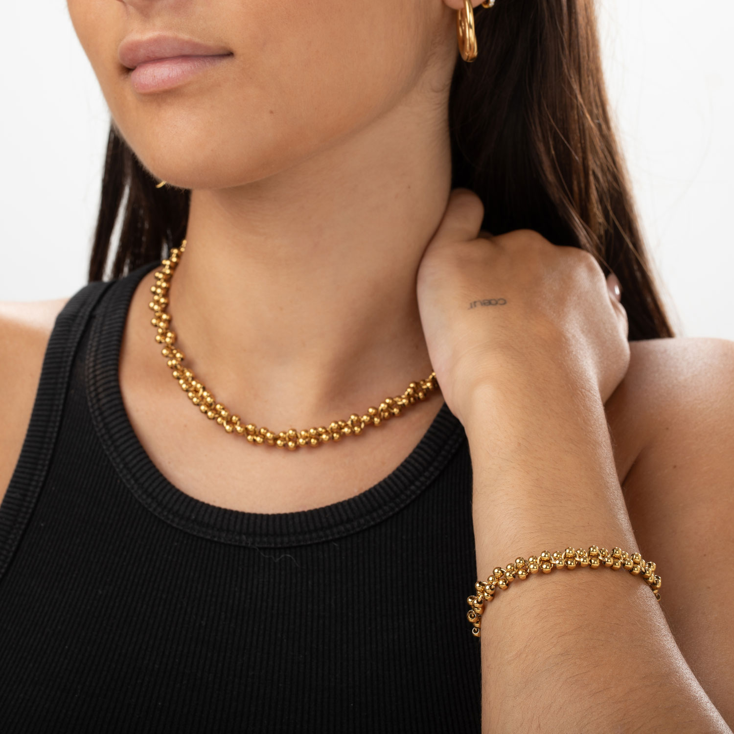 Colar e pulseira dourados em mulher com camiseta preta e tatuagem na mão