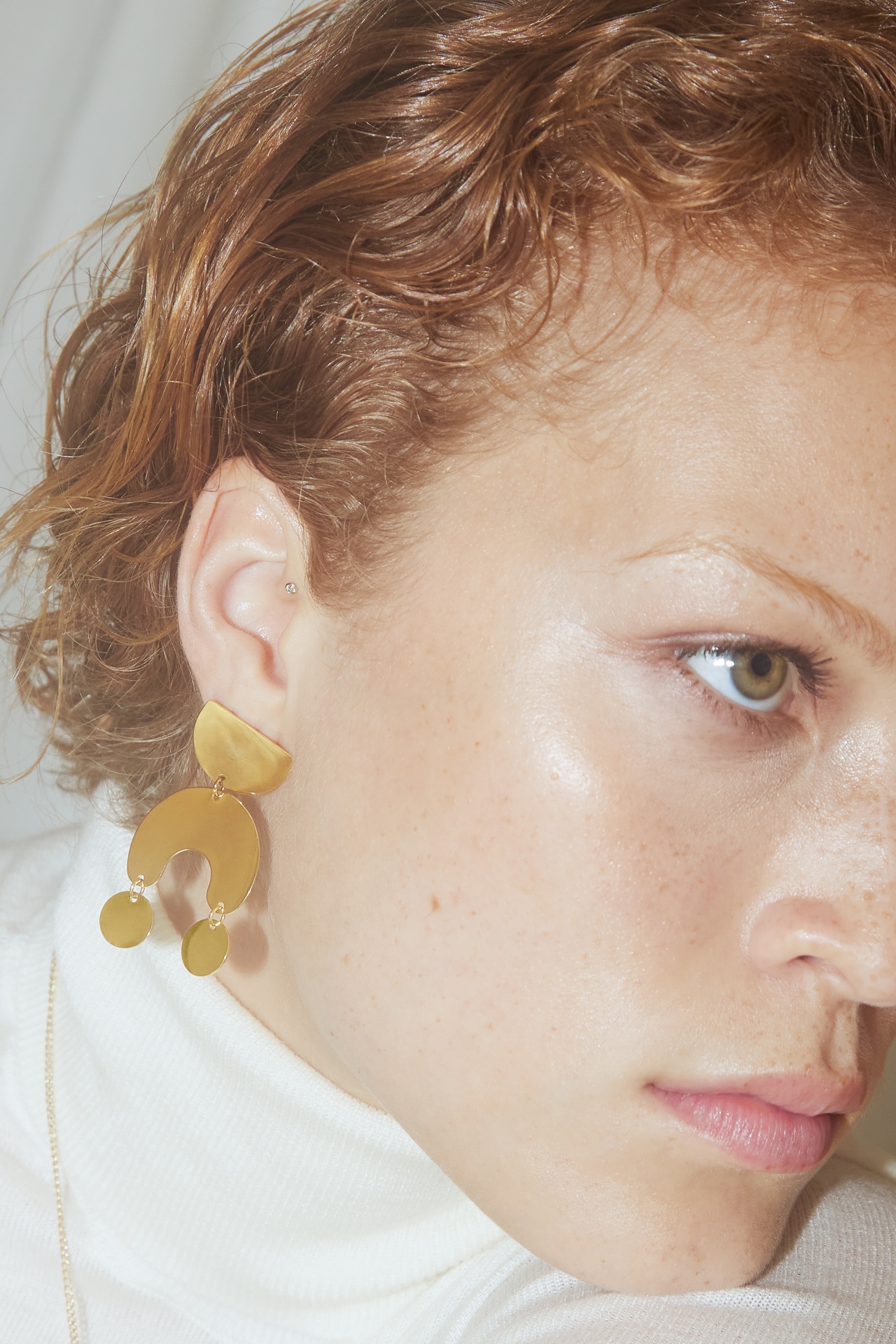 Brincos dourados geométricos usados por mulher com cabelo ruivo curto