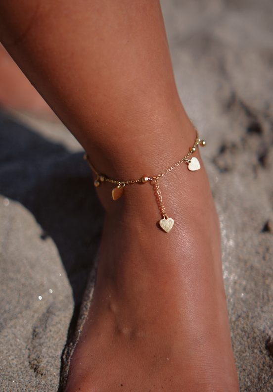 Tornozeleira dourada com corações num pé sobre areia