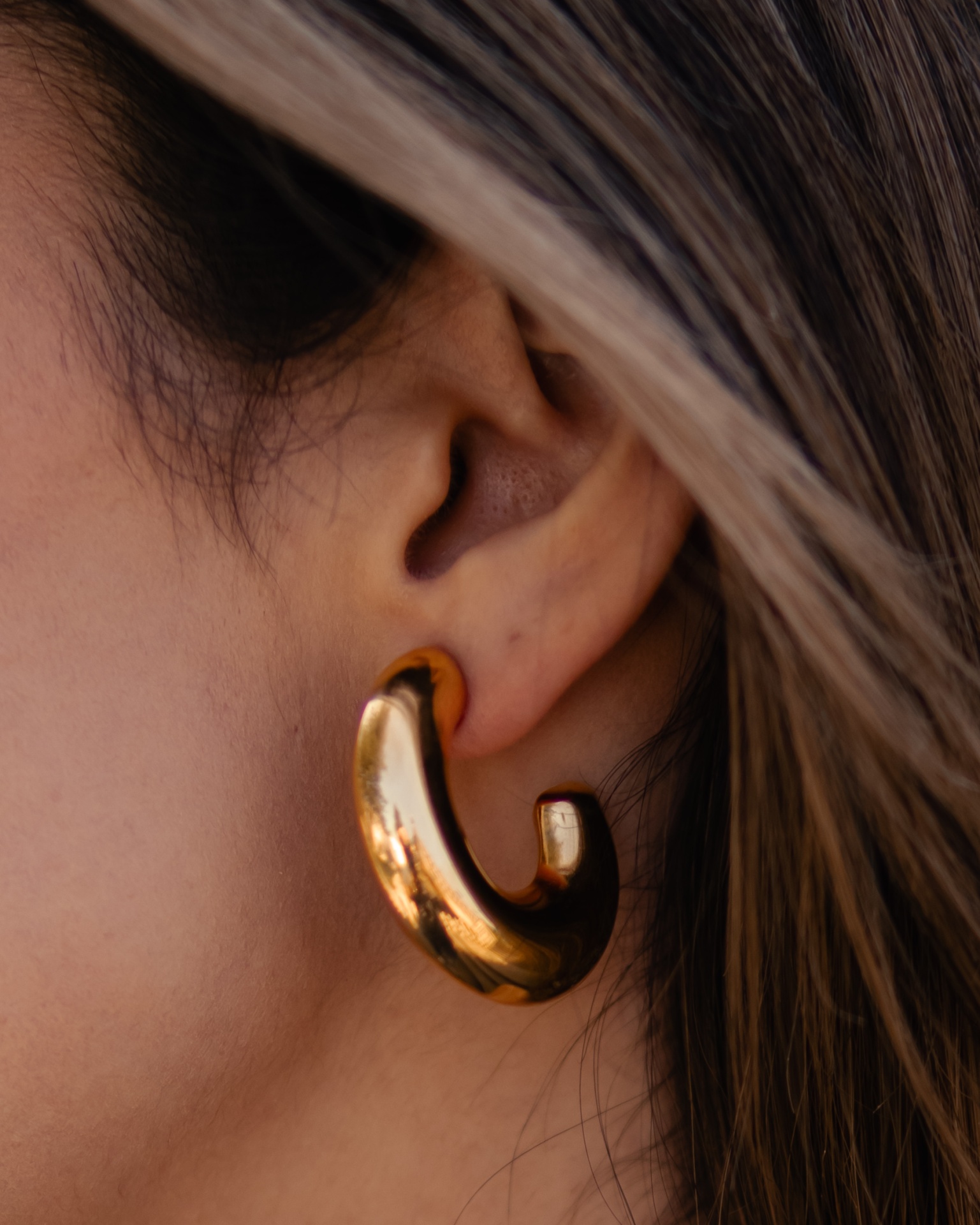 Brinco dourado em forma de argola grossa curvada na orelha