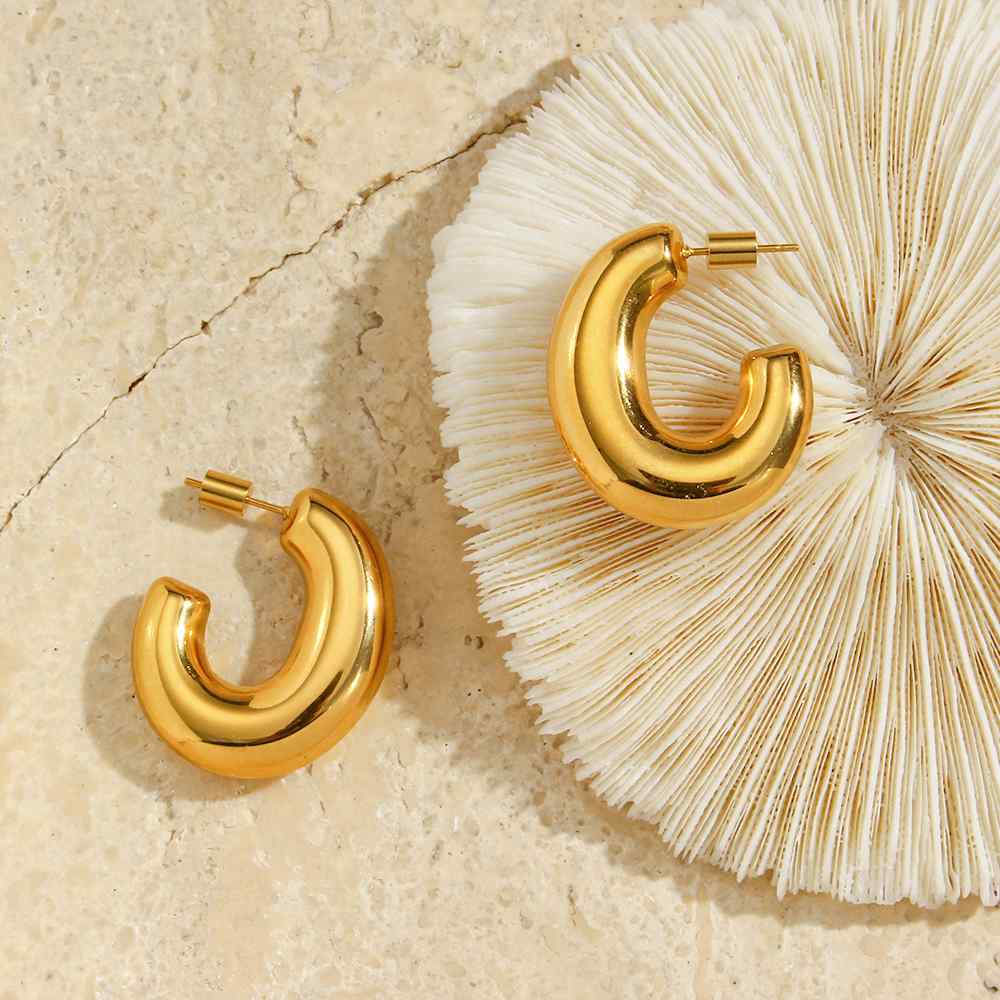 Brincos dourados tipo argola espessos sobre fundo claro e objeto branco texturado