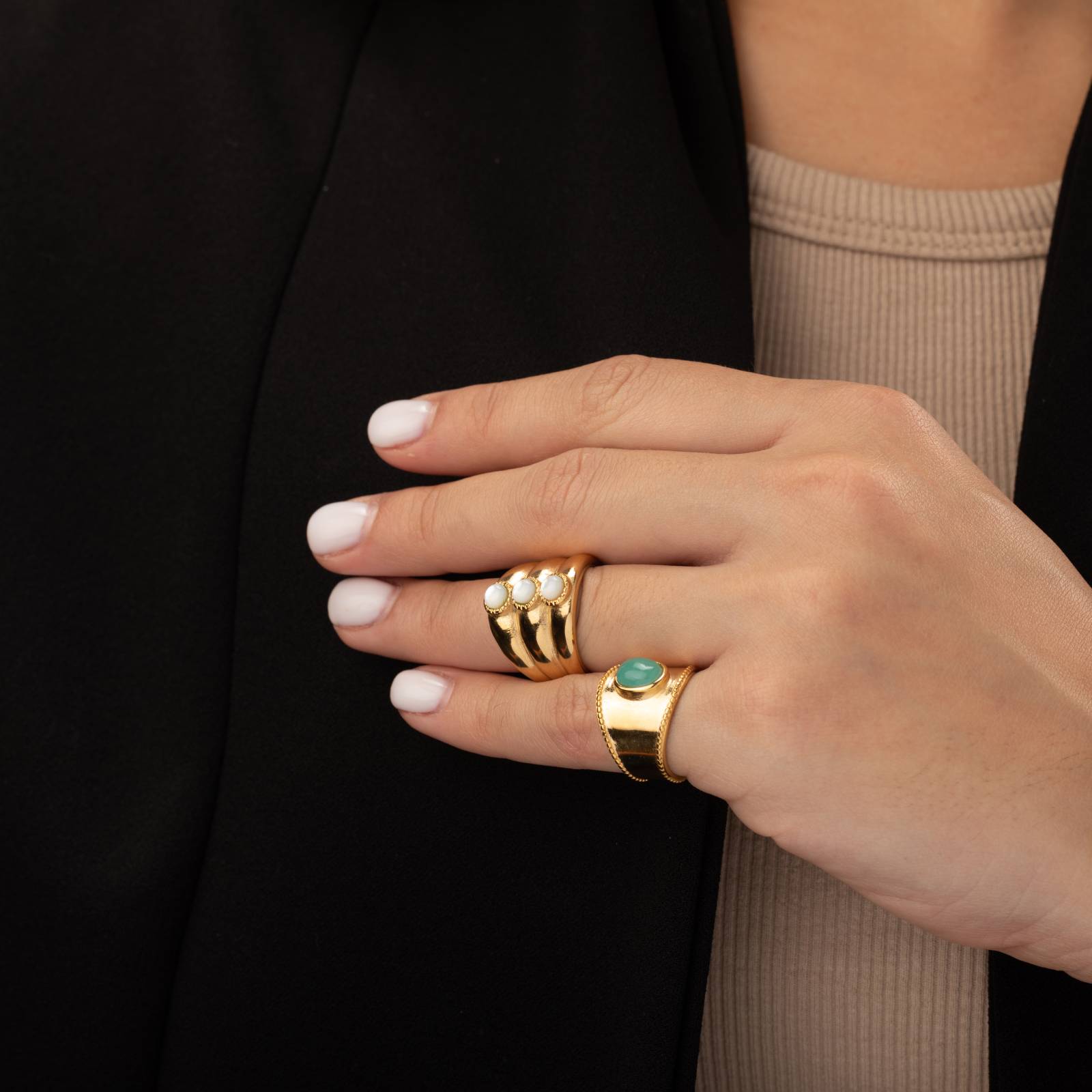 Anéis dourados com pérolas e pedra verde na mão feminina