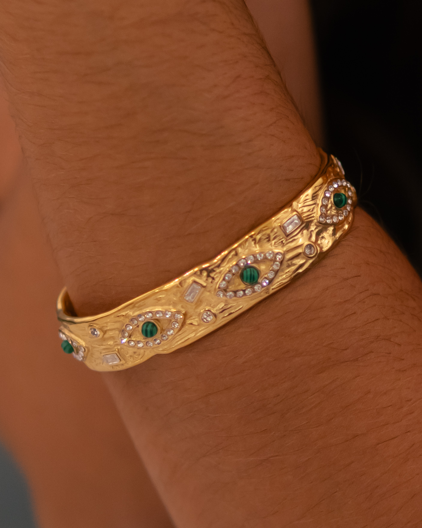 Pulseira dourada com pedras verdes num pulso