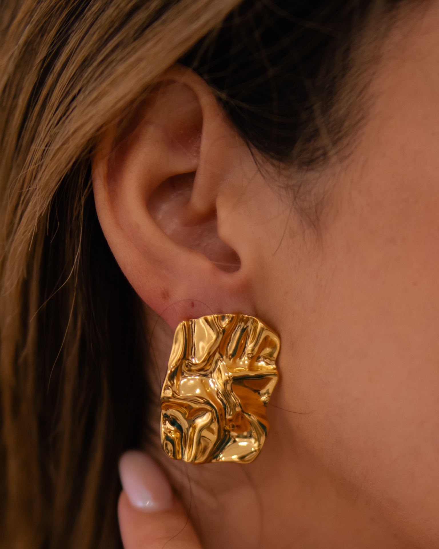 Brinco dourado texturizado na orelha de uma mulher