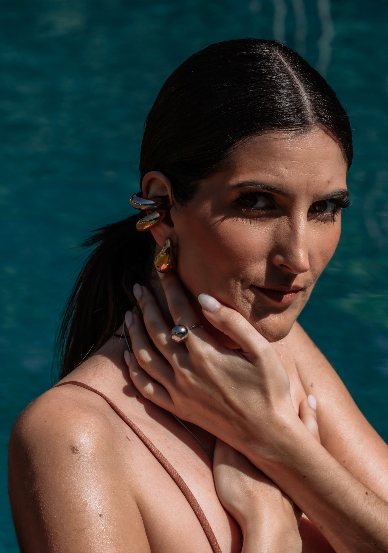 Mulher com brincos grandes, anel prateado, fundo de piscina verde-azulada