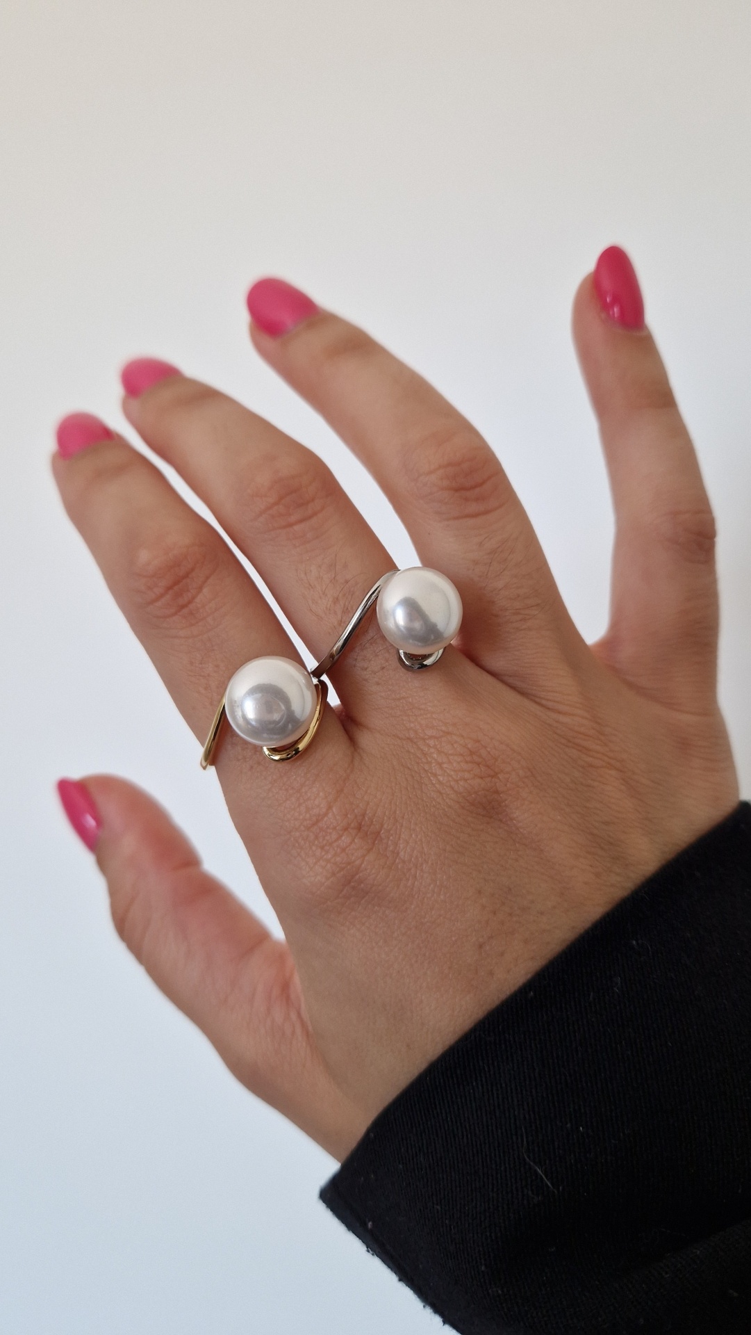 Anel com duas pérolas em metal dourado e prateado na mão com unhas rosas