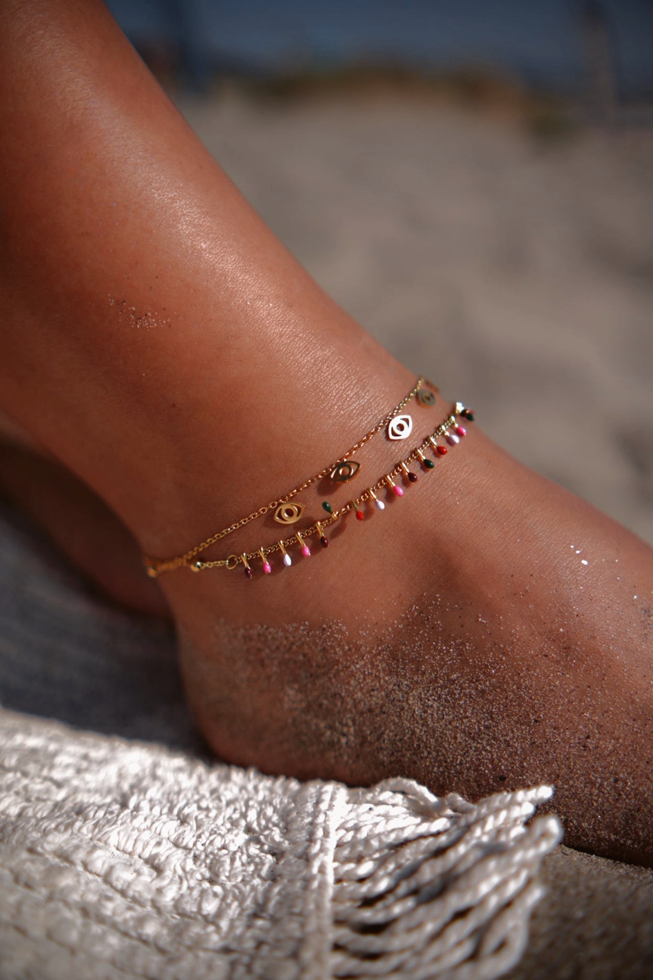 Tornozeleira dourada com pendentes ao redor de tornozelo bronzeado na areia