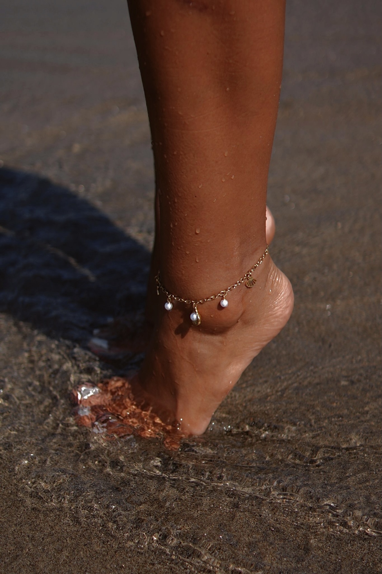 Tornozeleira dourada com pérolas num pé feminino na água