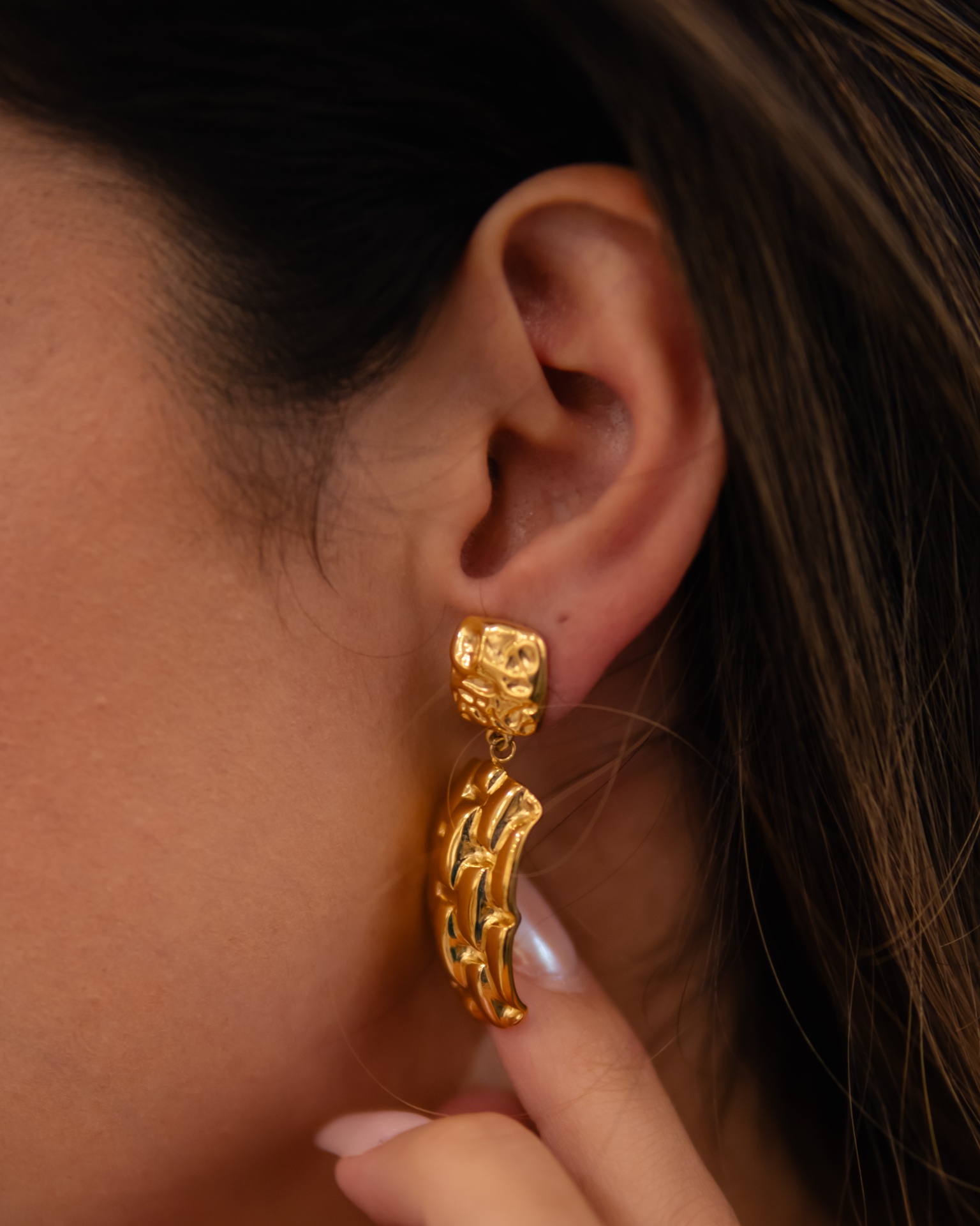 Brinco pendente dourado com textura geométrica na orelha de uma mulher