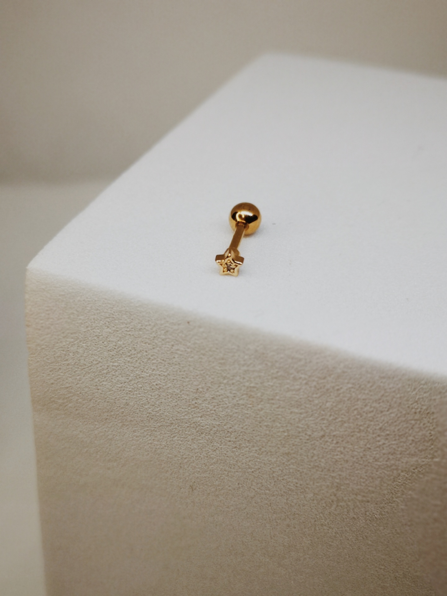 Piercing dourado com estrela numa superfície branca texturada.