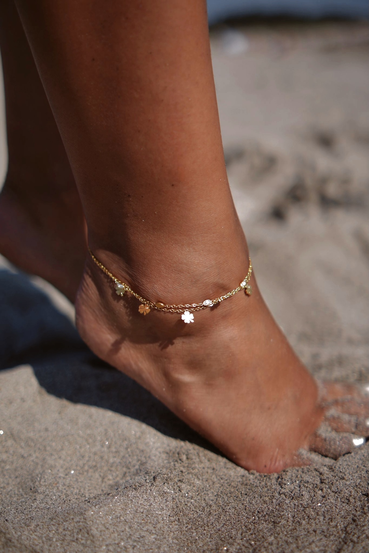 Tornozeleira dourada com pendentes em forma de flores e figuras circulares