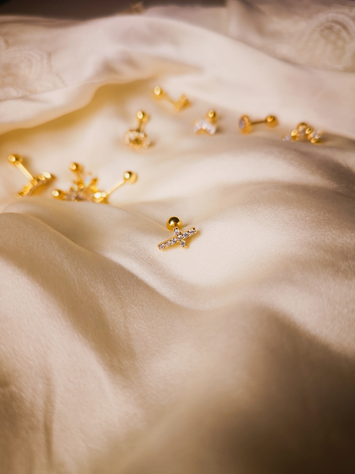 Vários brincos dourados com pedras sobre tecido branco de seda com bordado