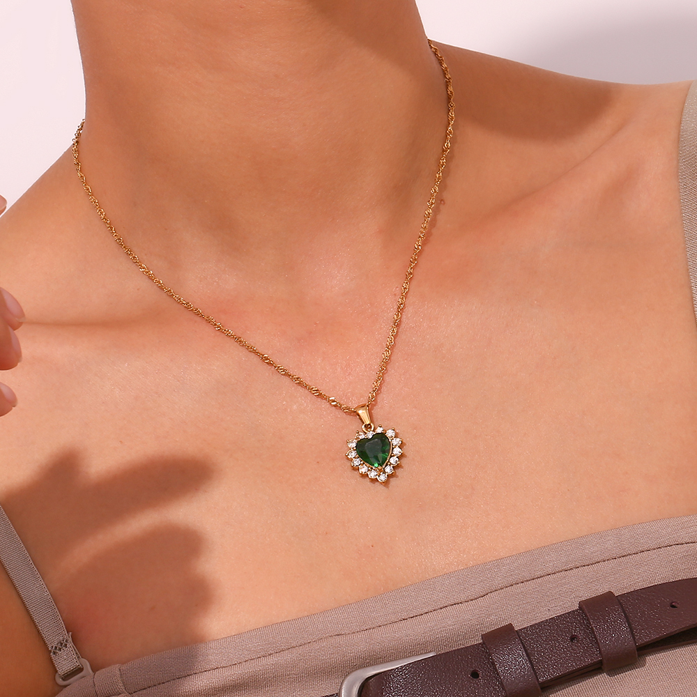 Colar dourado com pendente de coração verde rodeado de cristais brancos no pescoço de uma pessoa.