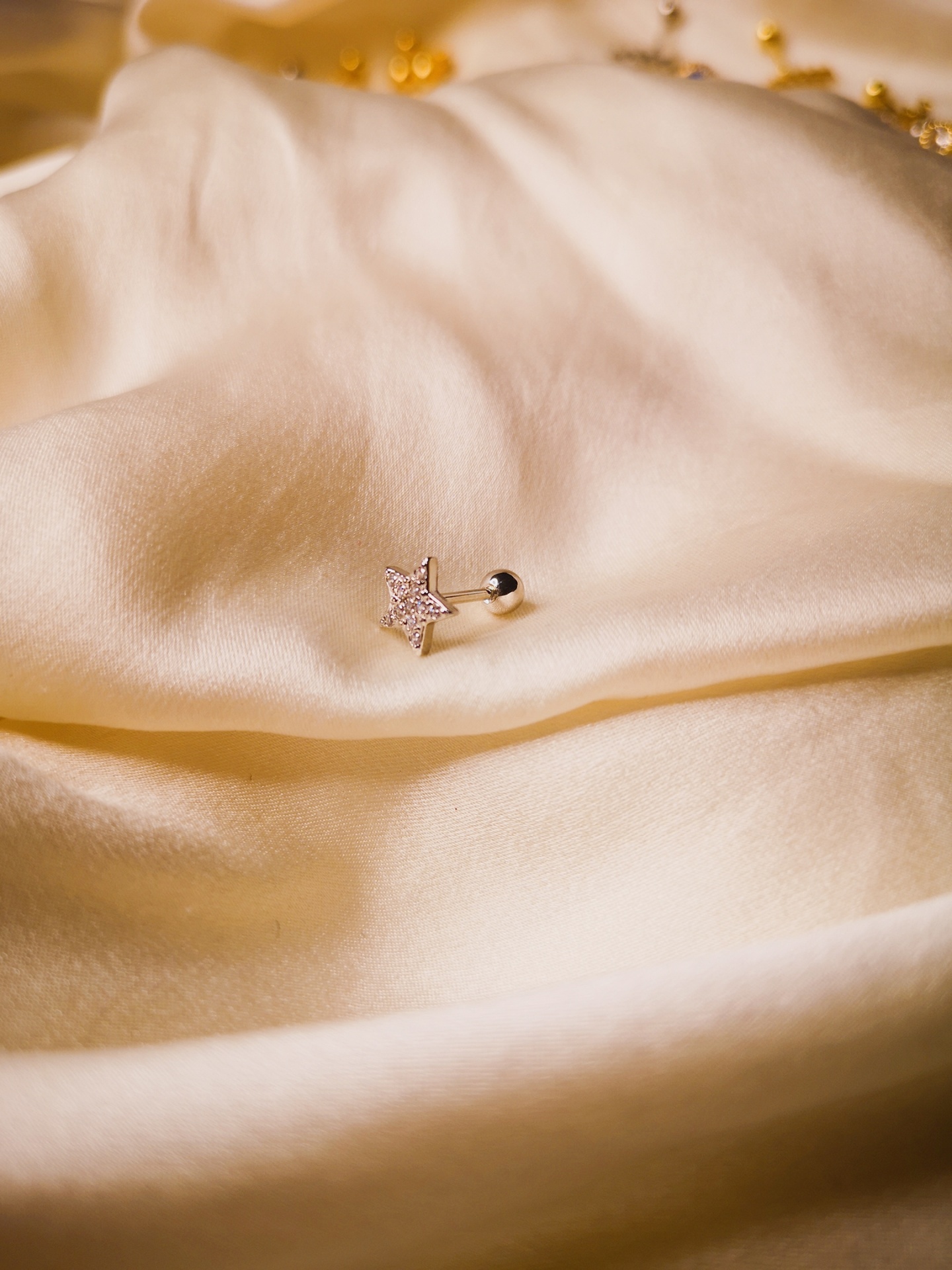 Brinco em forma de estrela prateada com brilhantes sobre tecido creme