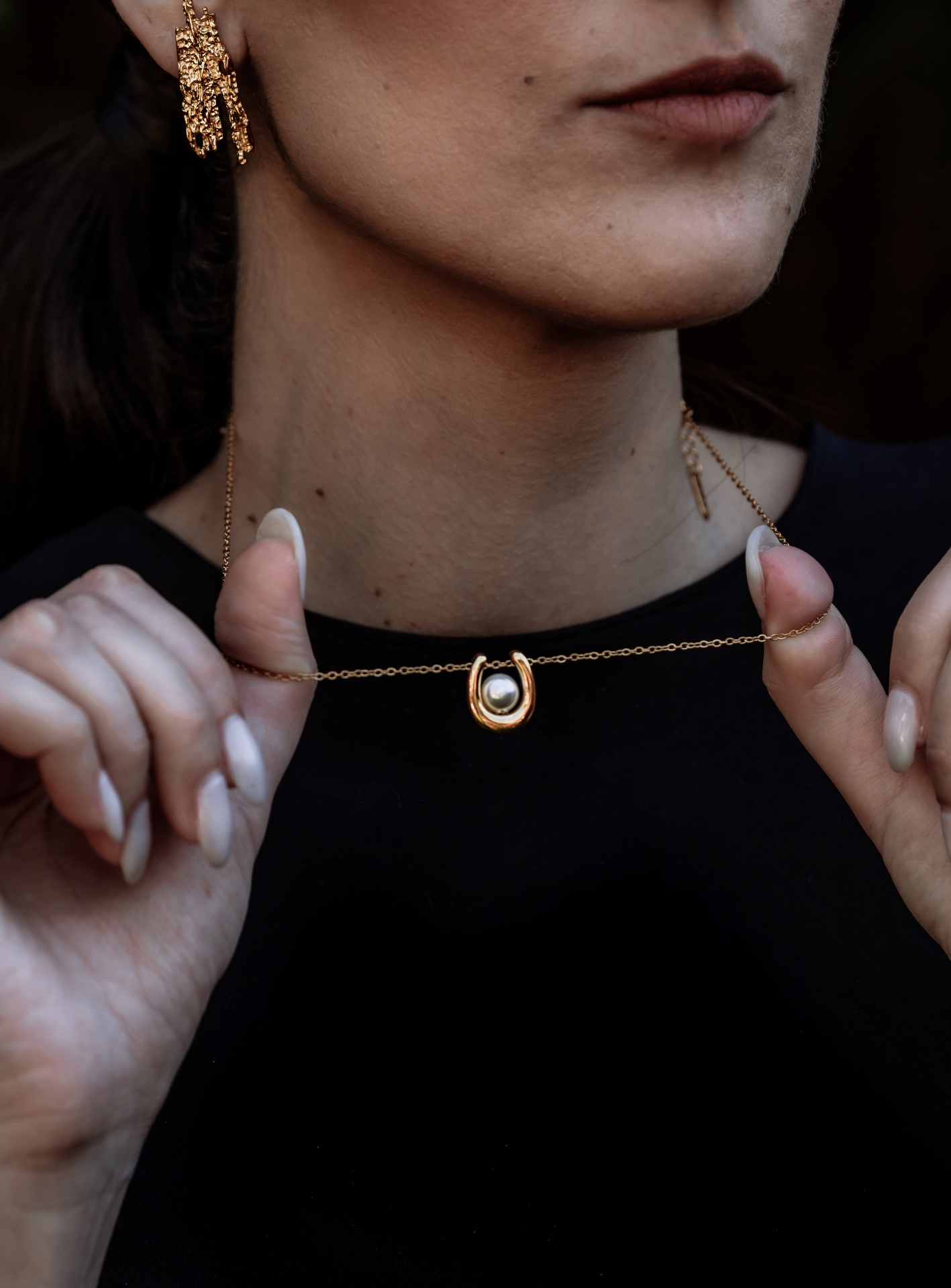 Mulher a segurar colar dourado com pendente de ferradura e pérola