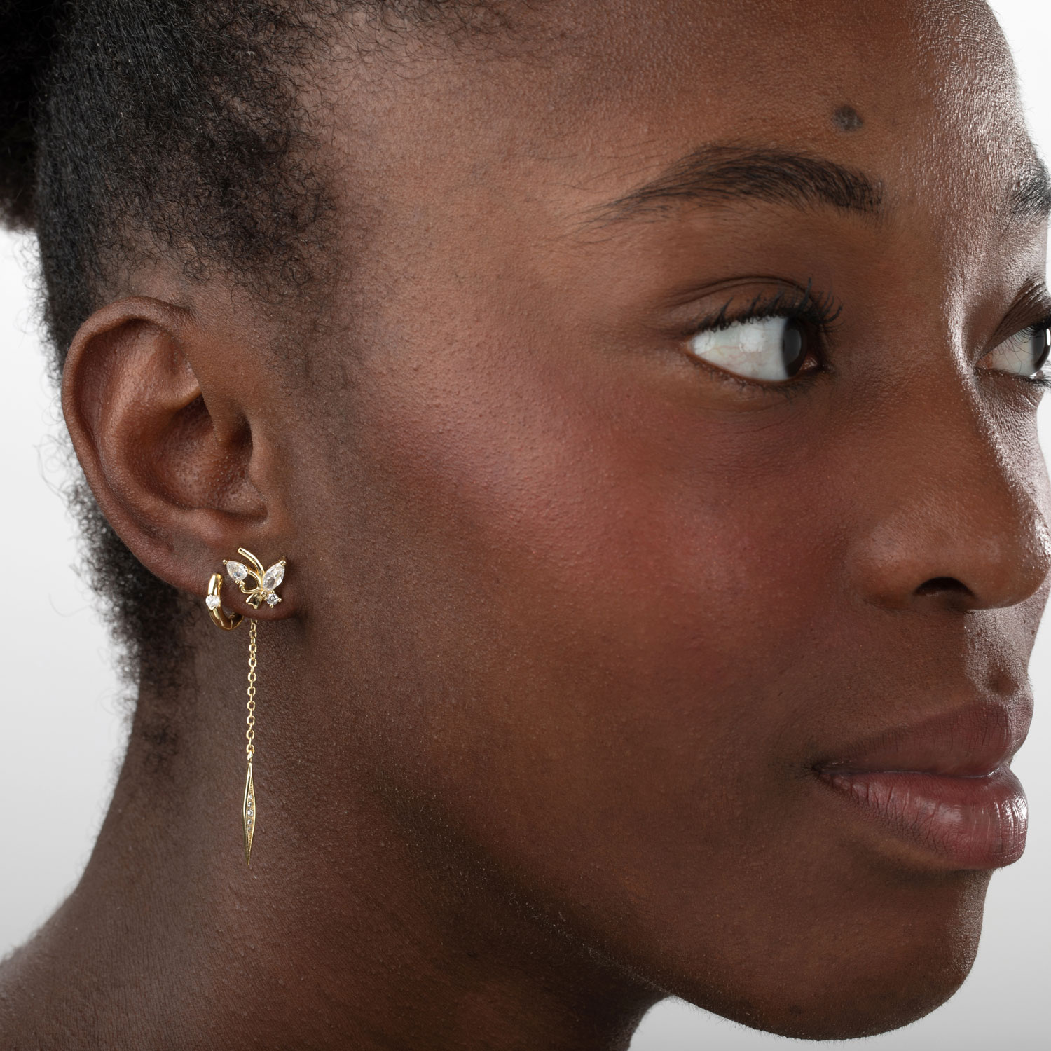 Brincos dourados em forma de folha e corrente pendente no ouvido de mulher