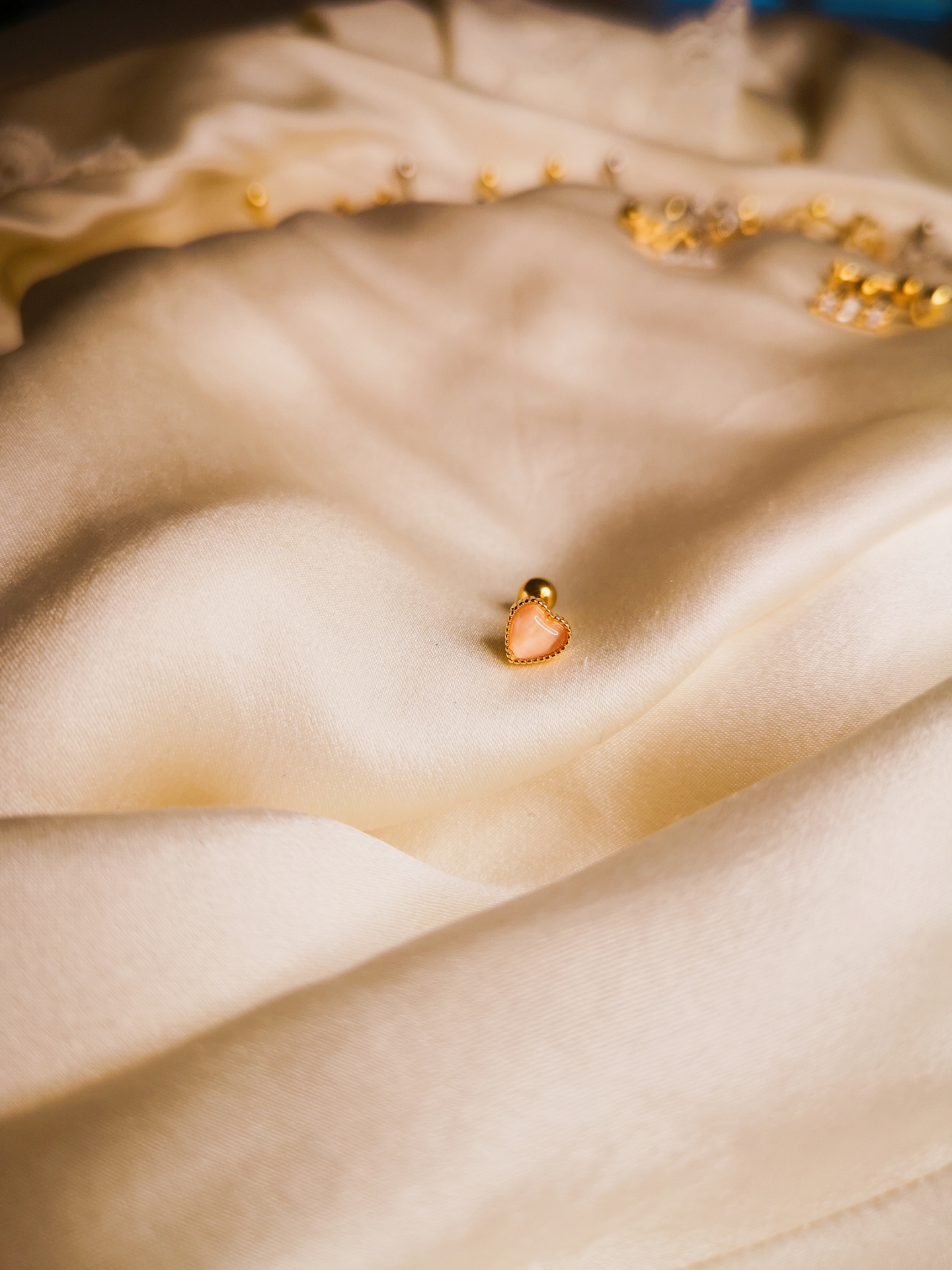 Brinco dourado com coração cor-de-rosa sobre tecido branco acetinado