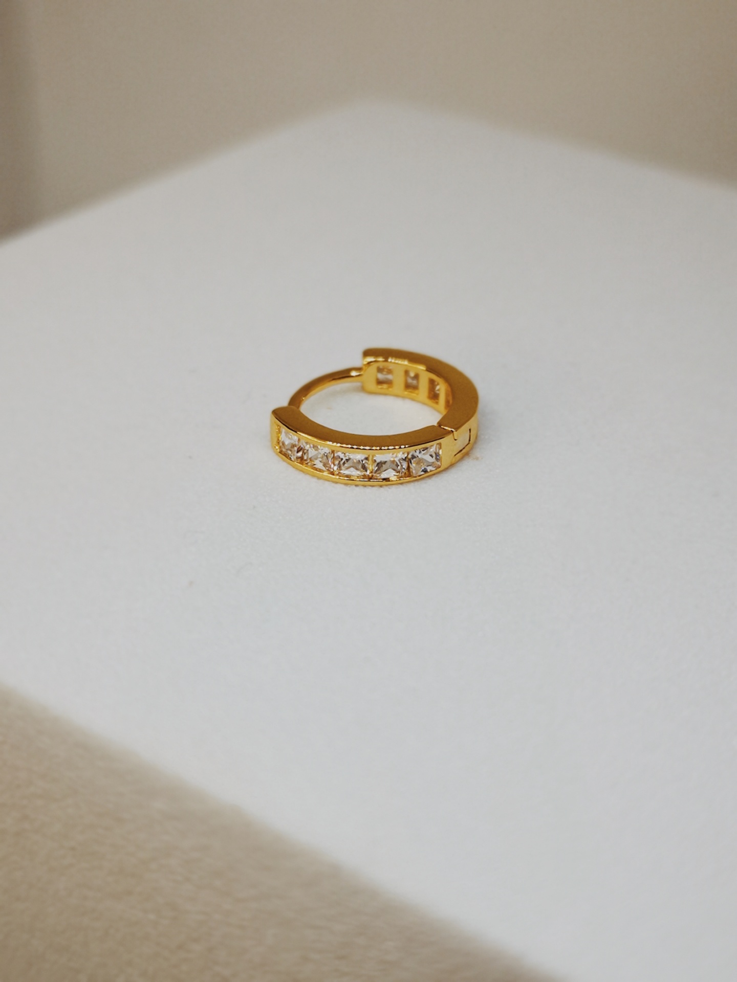 Argola dourada com pedras brilhantes sobre superfície branca