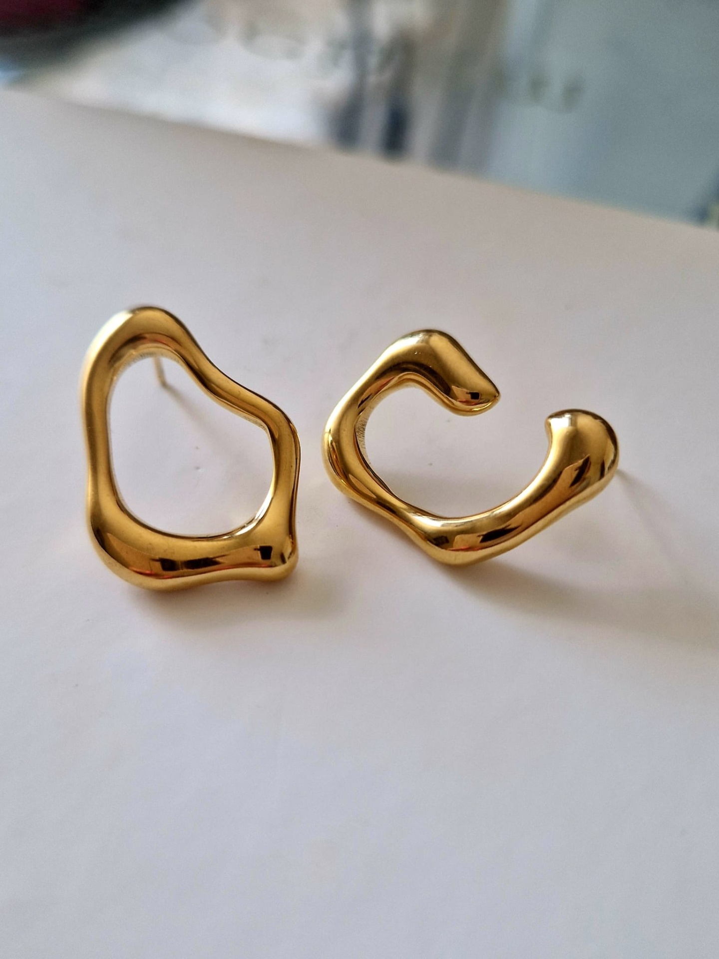 Brincos dourados de design irregular sobre superfície branca