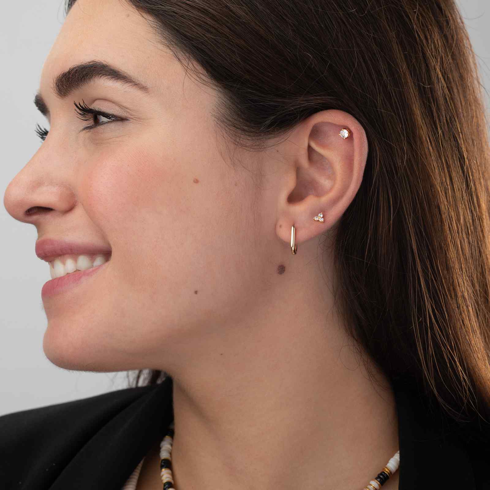 Mulher de perfil com brincos dourado e prata e colar de contas