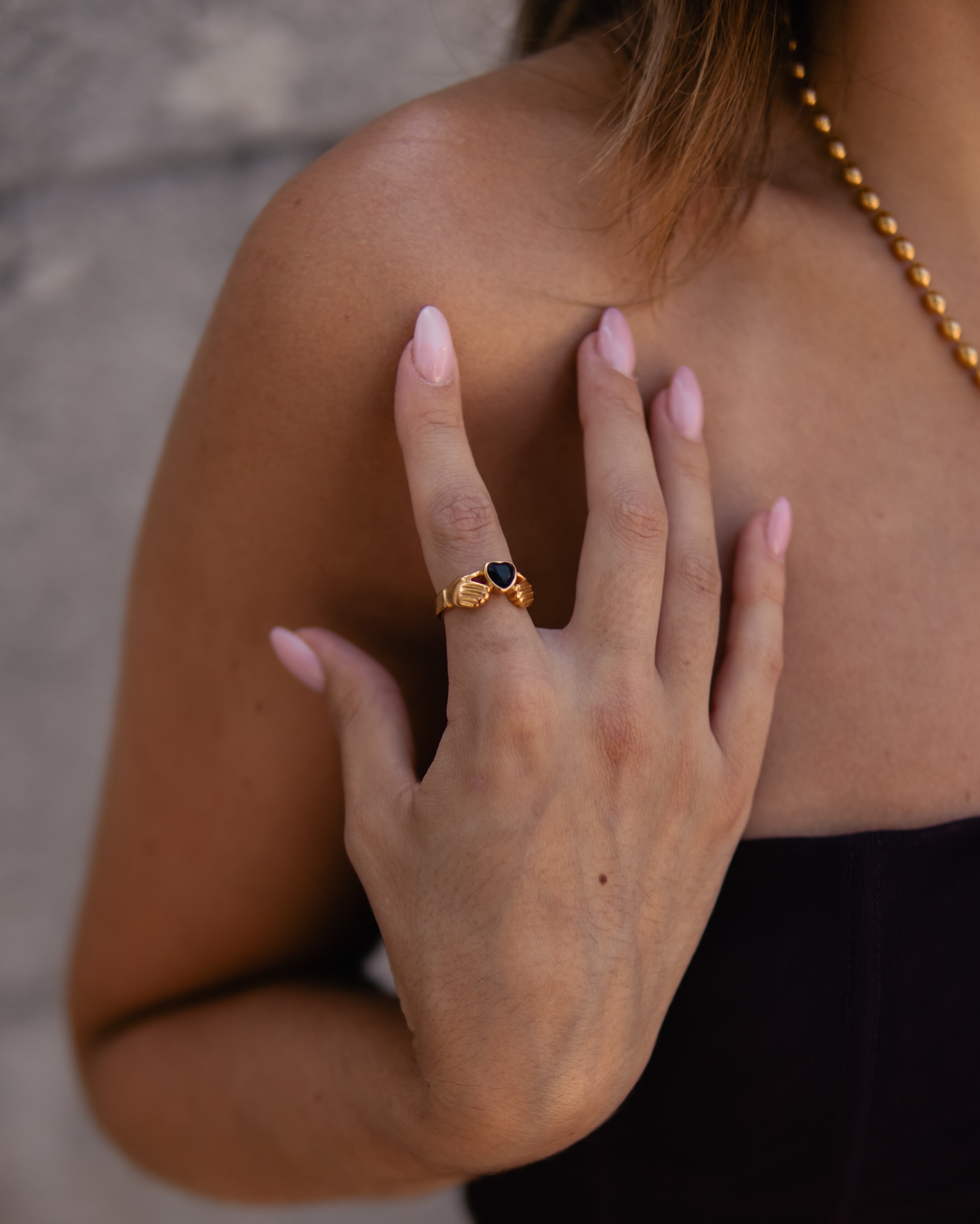 Anel dourado com pedra preta em forma de coração na mão de uma mulher