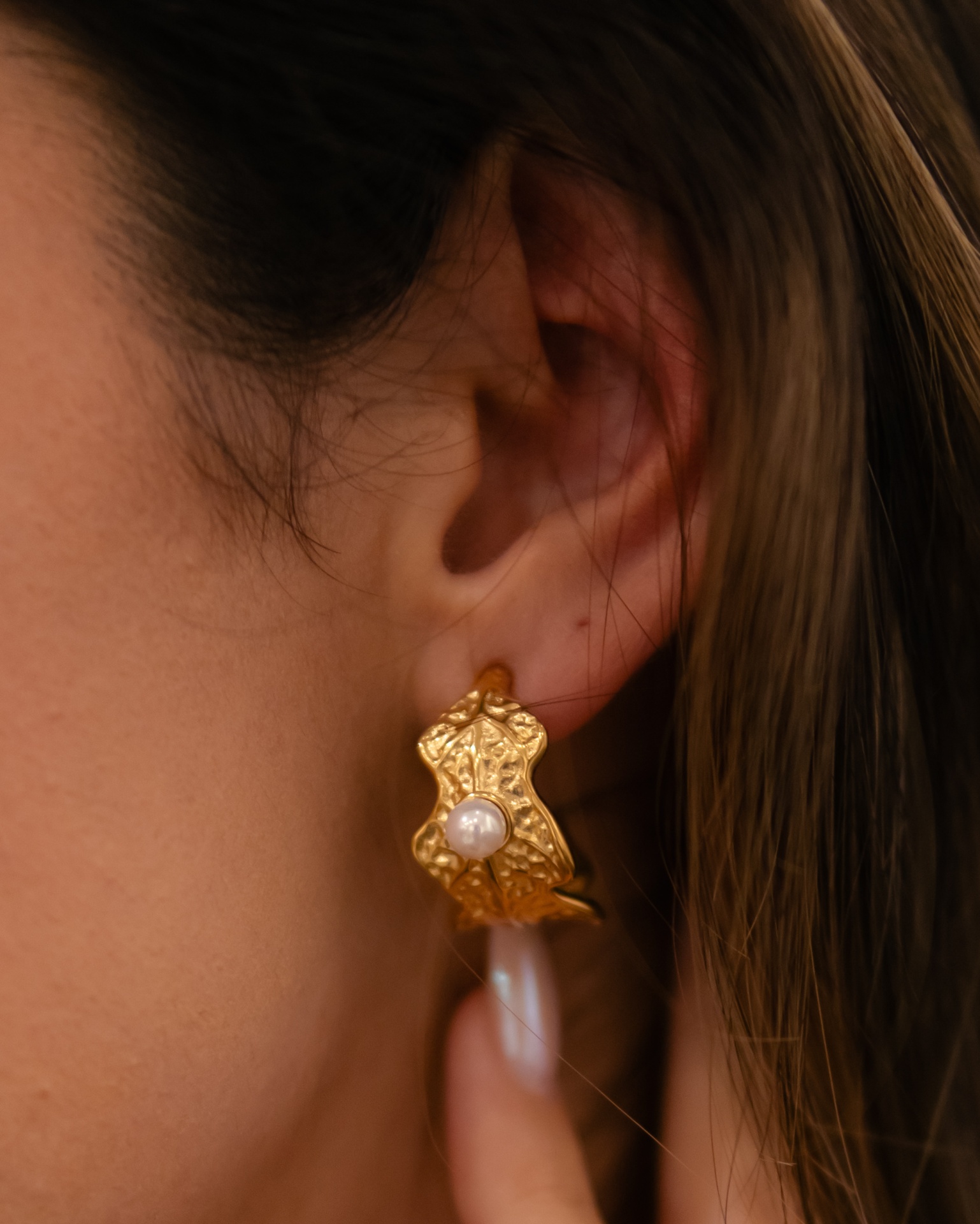Brinco dourado com pérola branca em orelha feminina