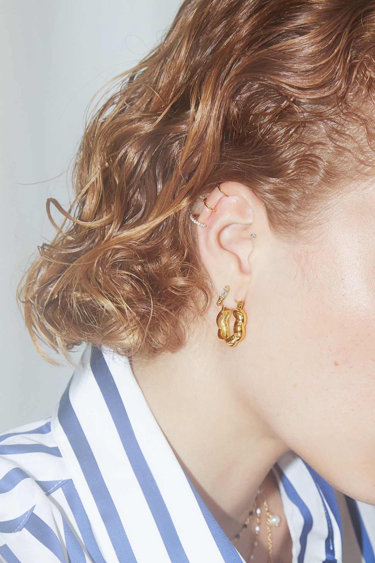 Orelha com vários brincos dourados e cabelo curto castanho claro