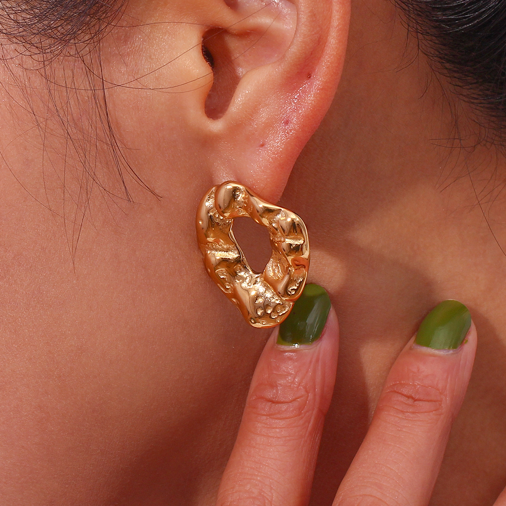 Brinco dourado orgânico em orelha com unhas verdes ao lado